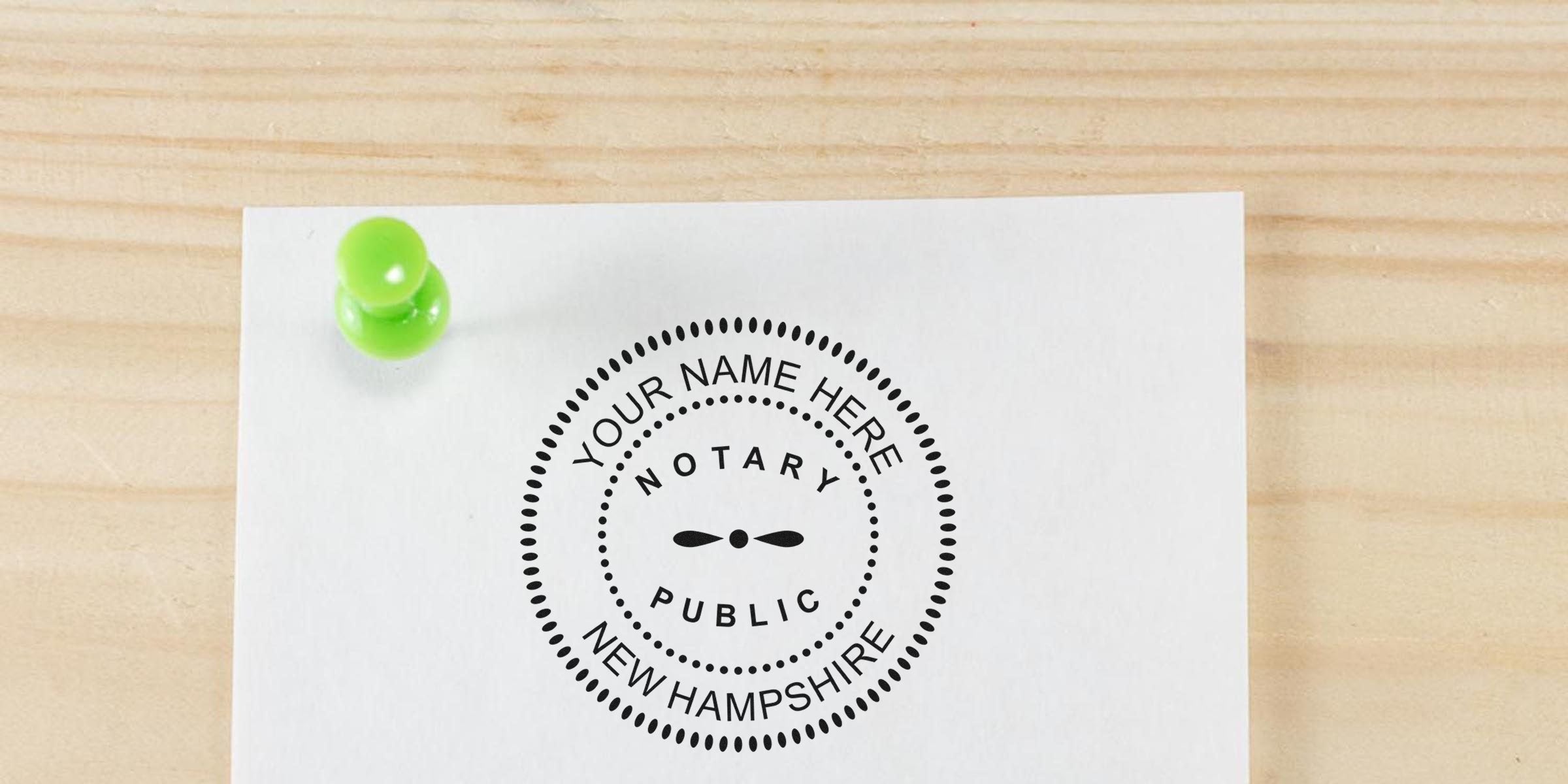 Round notary public seal reading "Your Name Here · Notary Public · New Hampshire" printed on white paper, secured with a bright green push pin on a light wood background.