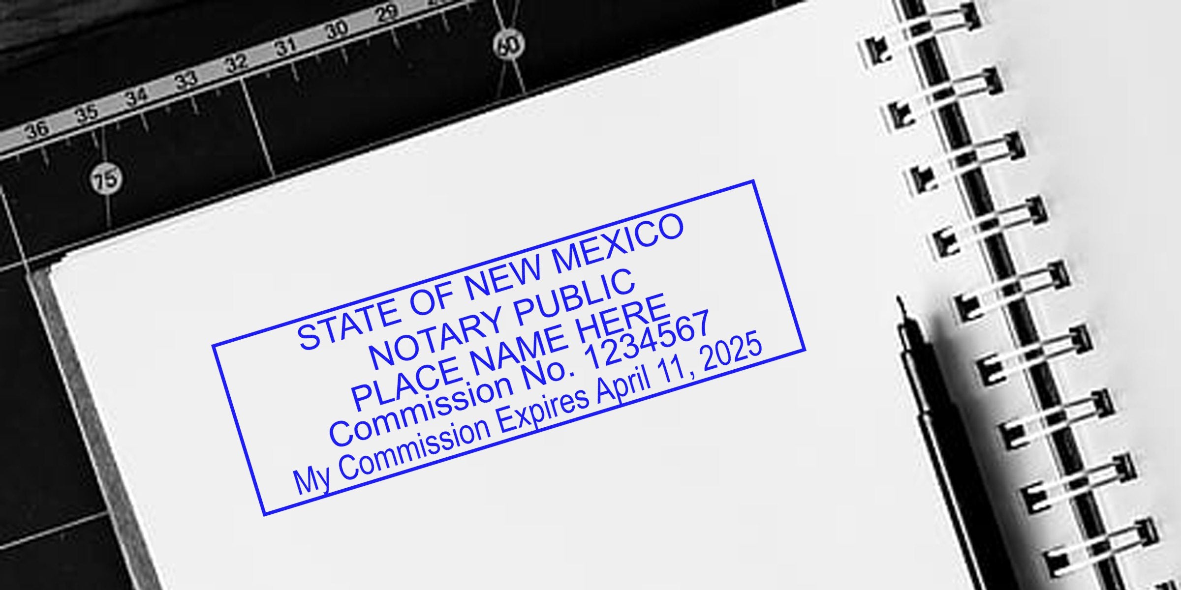 Blue "State of New Mexico Notary Public" stamp mockup on white spiral notebook page, with black pen and cutting mat ruler nearby