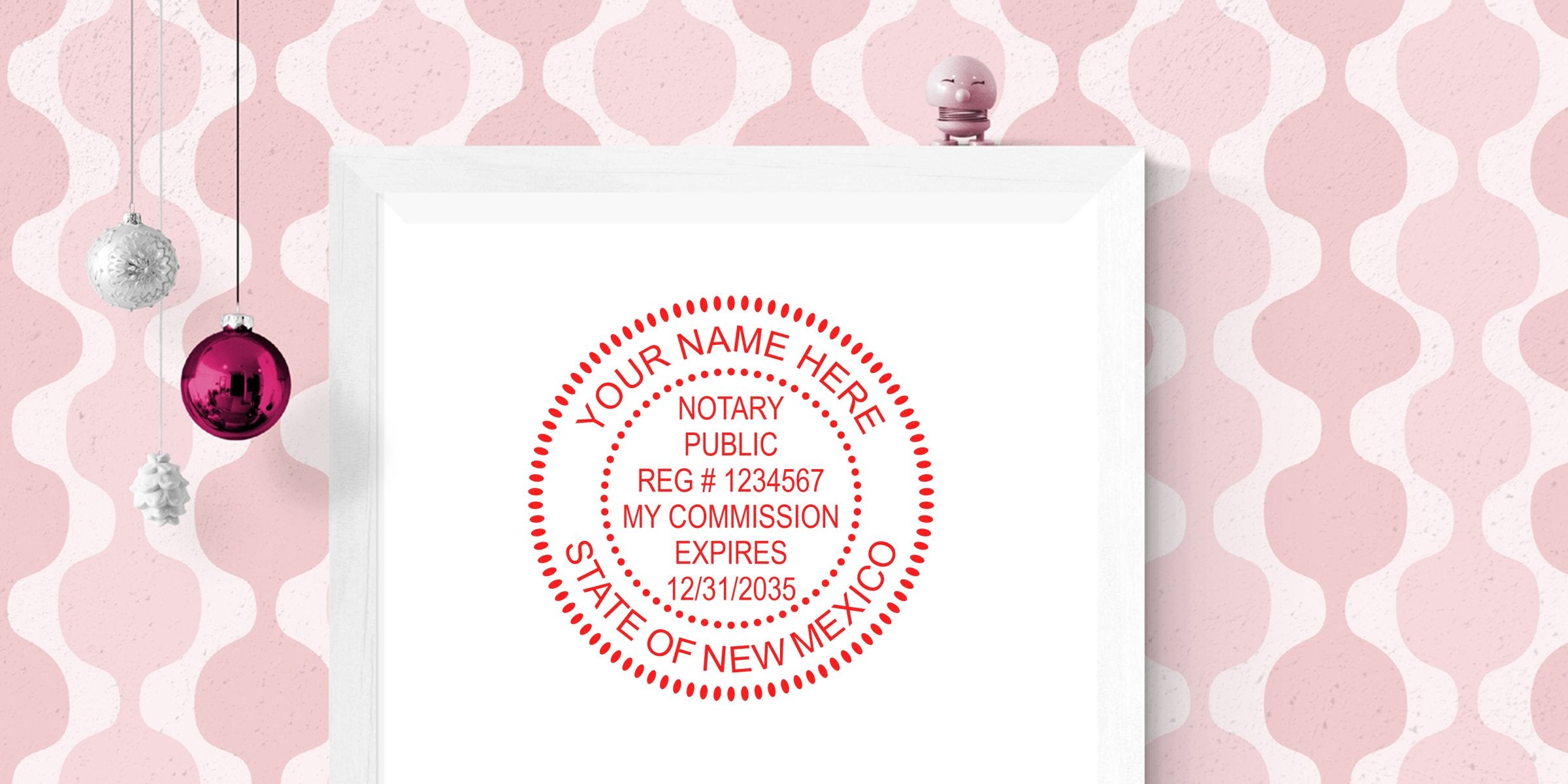 Framed white print with red circular notary public stamp reading "Your Name Here" and "State of New Mexico" on pink retro patterned wall with hanging ornaments.