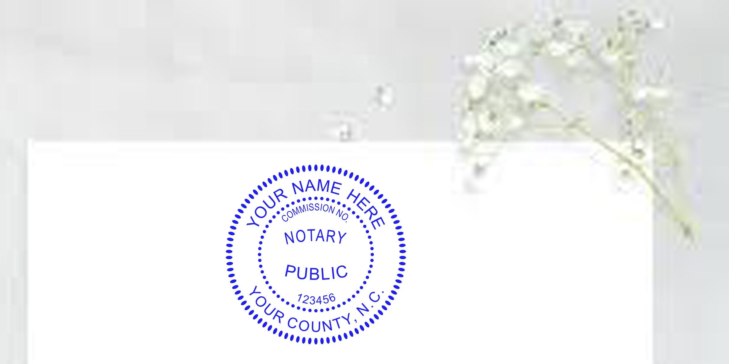 Blue circular notary public stamp with placeholder text "Your Name Here", commission number and county on white paper, delicate lily-of-the-valley sprig on a soft gray background
