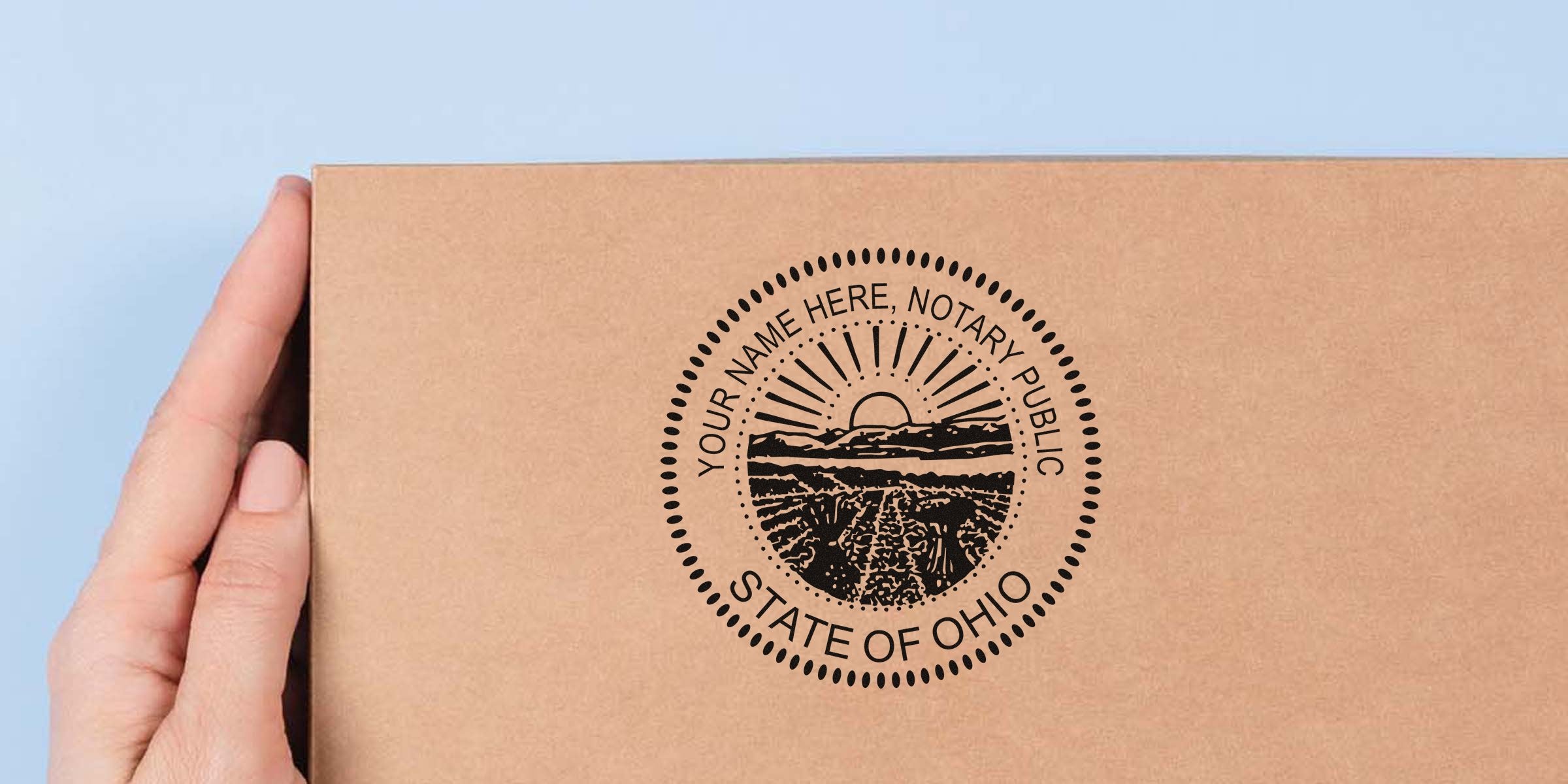 Hand holding kraft cardboard box stamped with round "State of Ohio" notary public seal featuring sunrise over fields and dotted border.