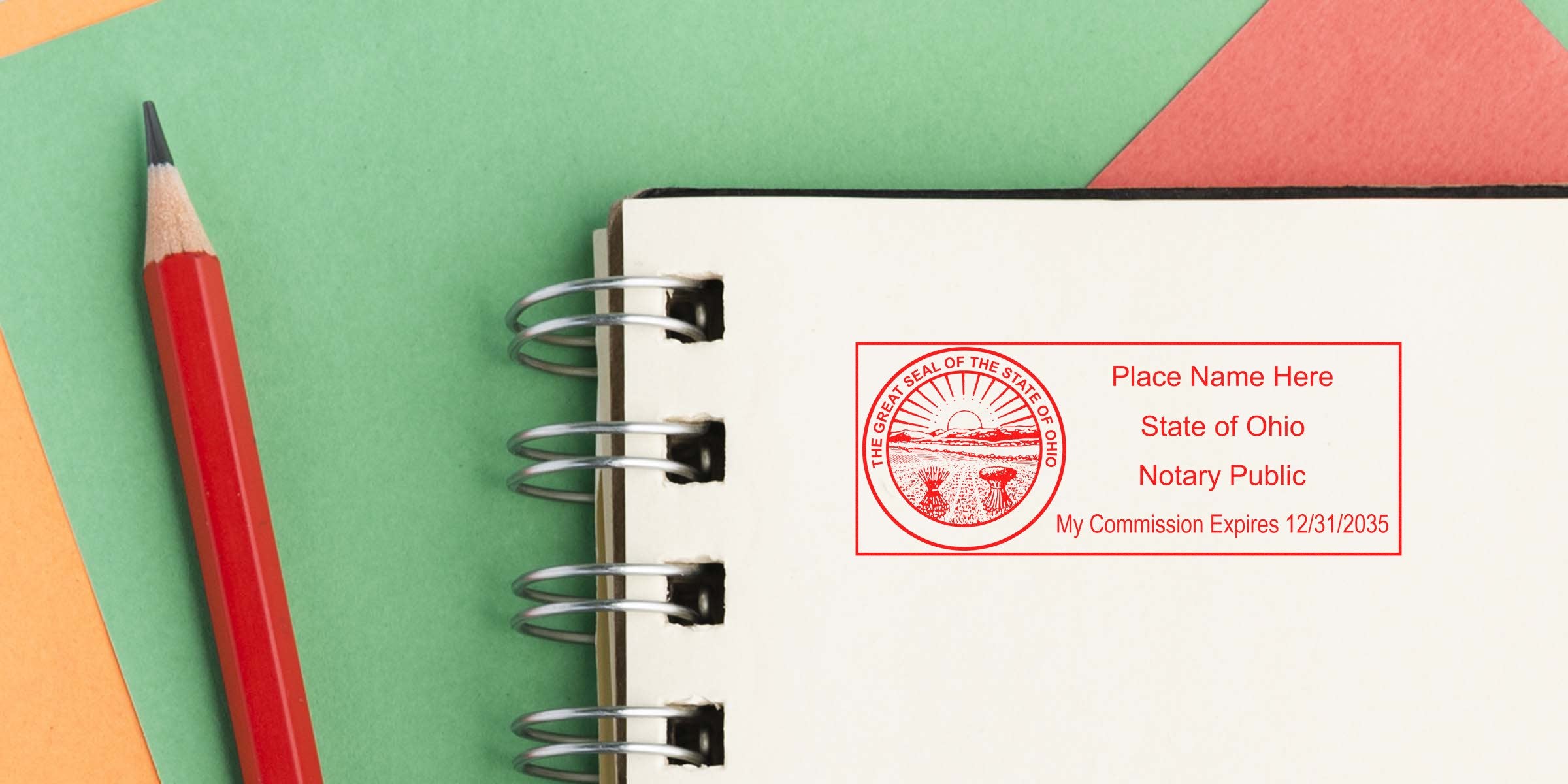 Spiral notebook open to blank page with red Ohio notary public stamp and expiration date, red pencil on green and orange paper background