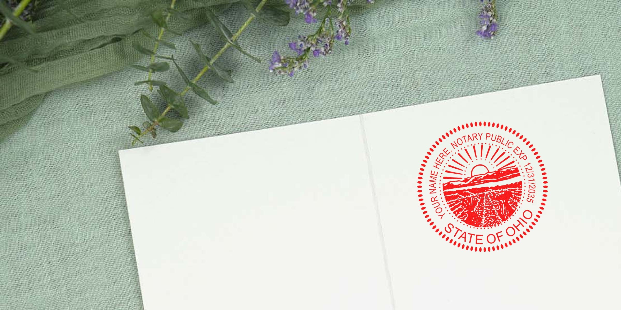 Red circular State of Ohio notary public seal stamped in red ink on white folded card, placed on green linen fabric with eucalyptus sprigs and small purple flowers.