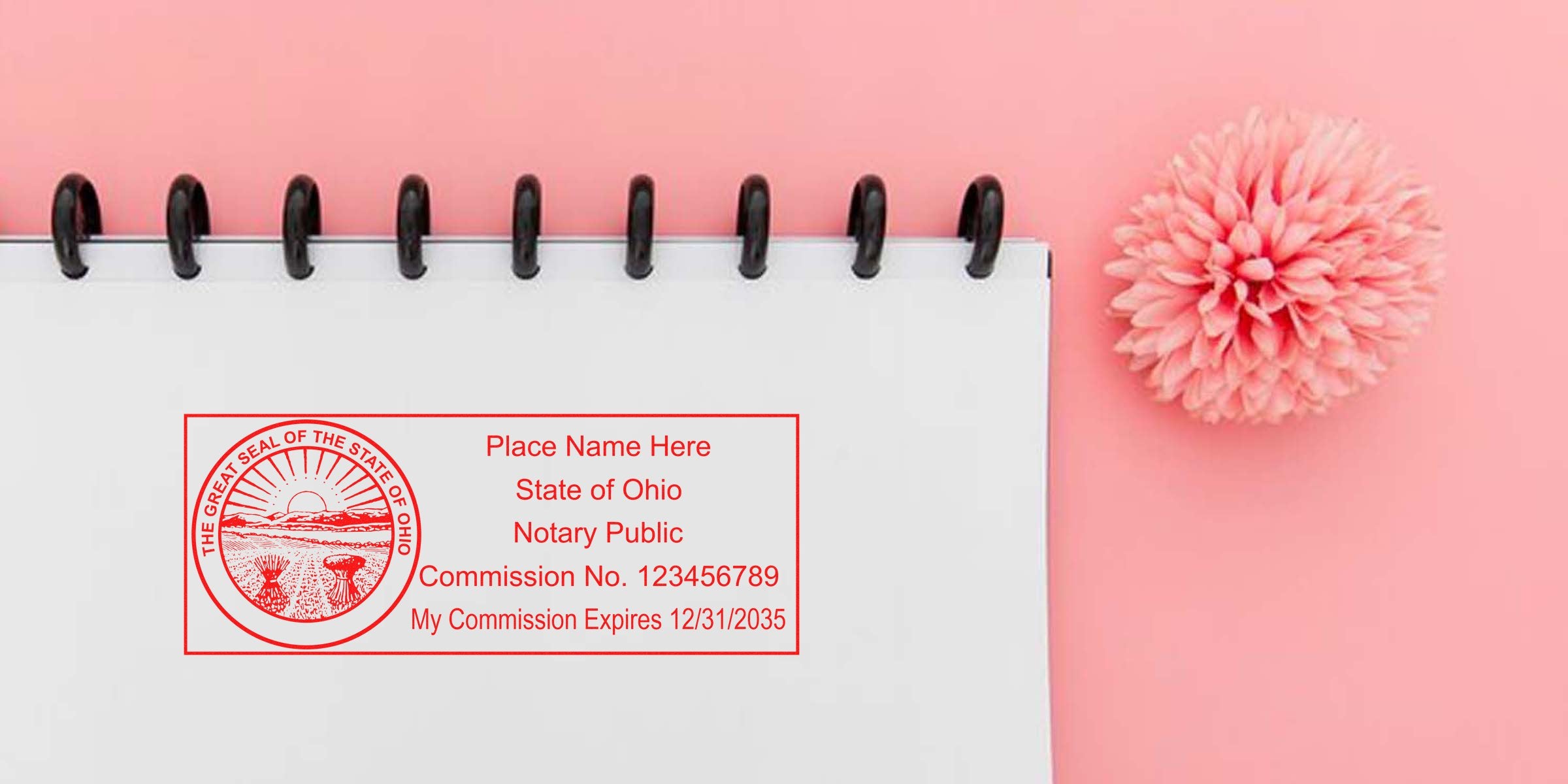 Red Ohio notary public stamp impression on white spiral-bound notebook against pink background with decorative pink pom-pom flower; customizable name, commission number and expiration date visible.