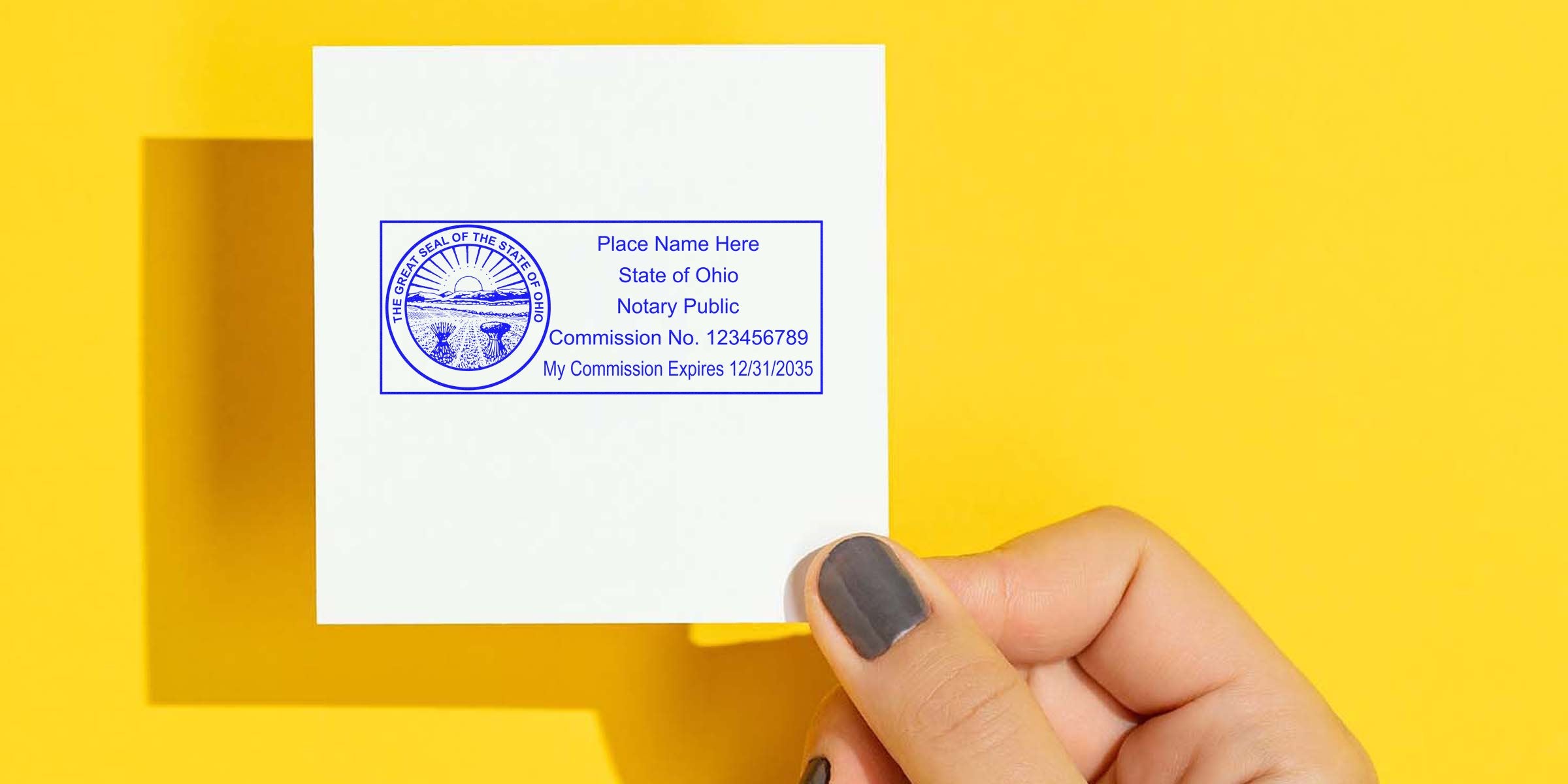 Hand holding small white card with blue Ohio notary public stamp and seal showing commission number and expiration on yellow background