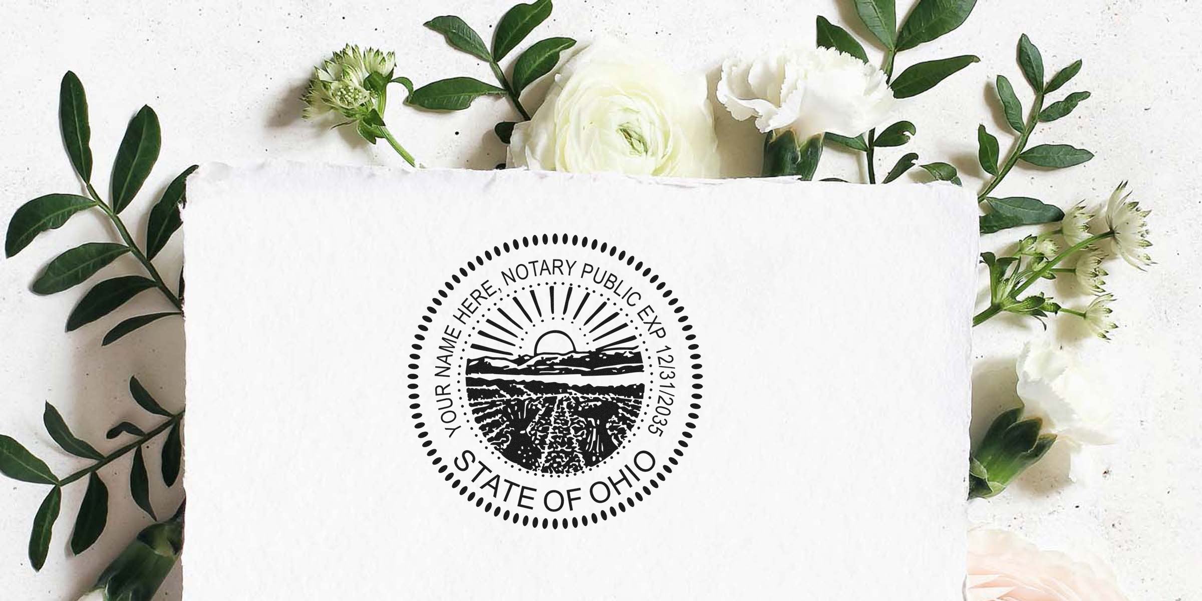 Ohio notary public round seal stamp mockup on textured white paper, black circular notary design with sunrise and fields, surrounded by white flowers and green foliage