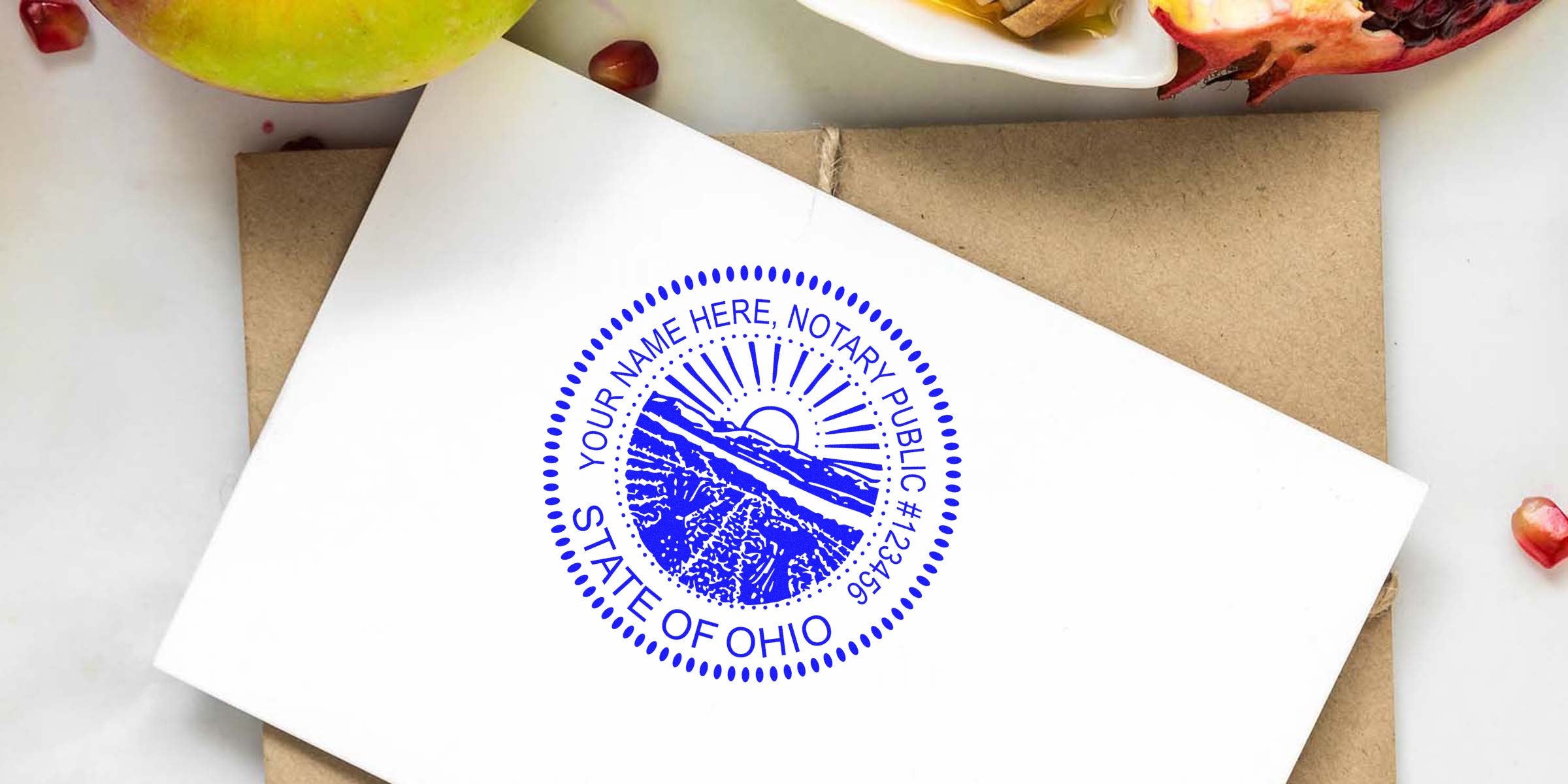 Blue circular "State of Ohio" notary public seal stamped on white card, shown with kraft envelope, green apple and pomegranate seeds — close-up product photo for notary stamp, stationery or legal office supplies.