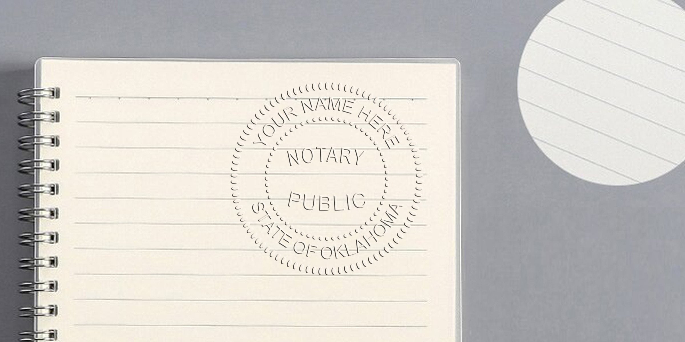 Open spiral-bound lined notebook with an embossed "Notary Public, State of Oklahoma" circular seal on cream paper against a gray desk and round white notepad.