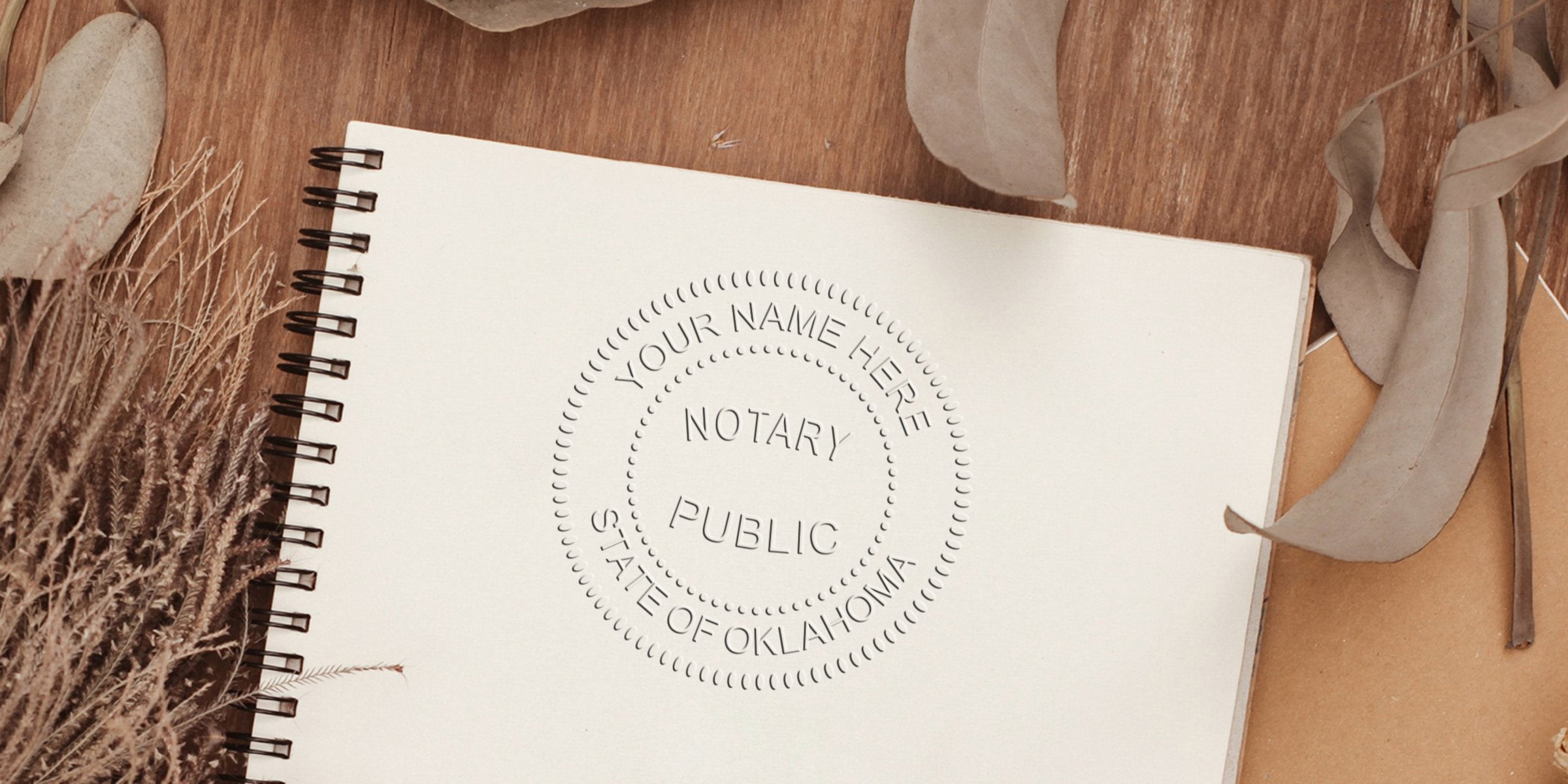 Spiral-bound notebook on wooden table with embossed "Notary Public • State of Oklahoma • Your Name Here" seal, surrounded by dried leaves and grasses