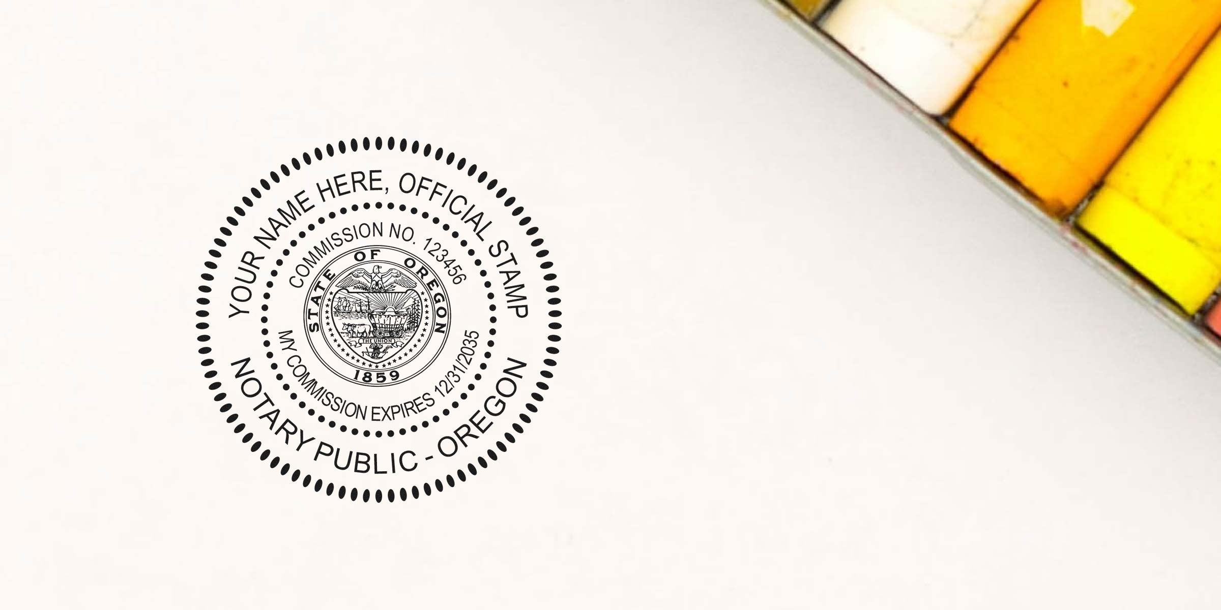 Black circular Oregon notary public stamp on white paper featuring state seal, commission number and expiration date, placeholder "Your Name Here" text; yellow and orange chalk pastels visible at top-right.