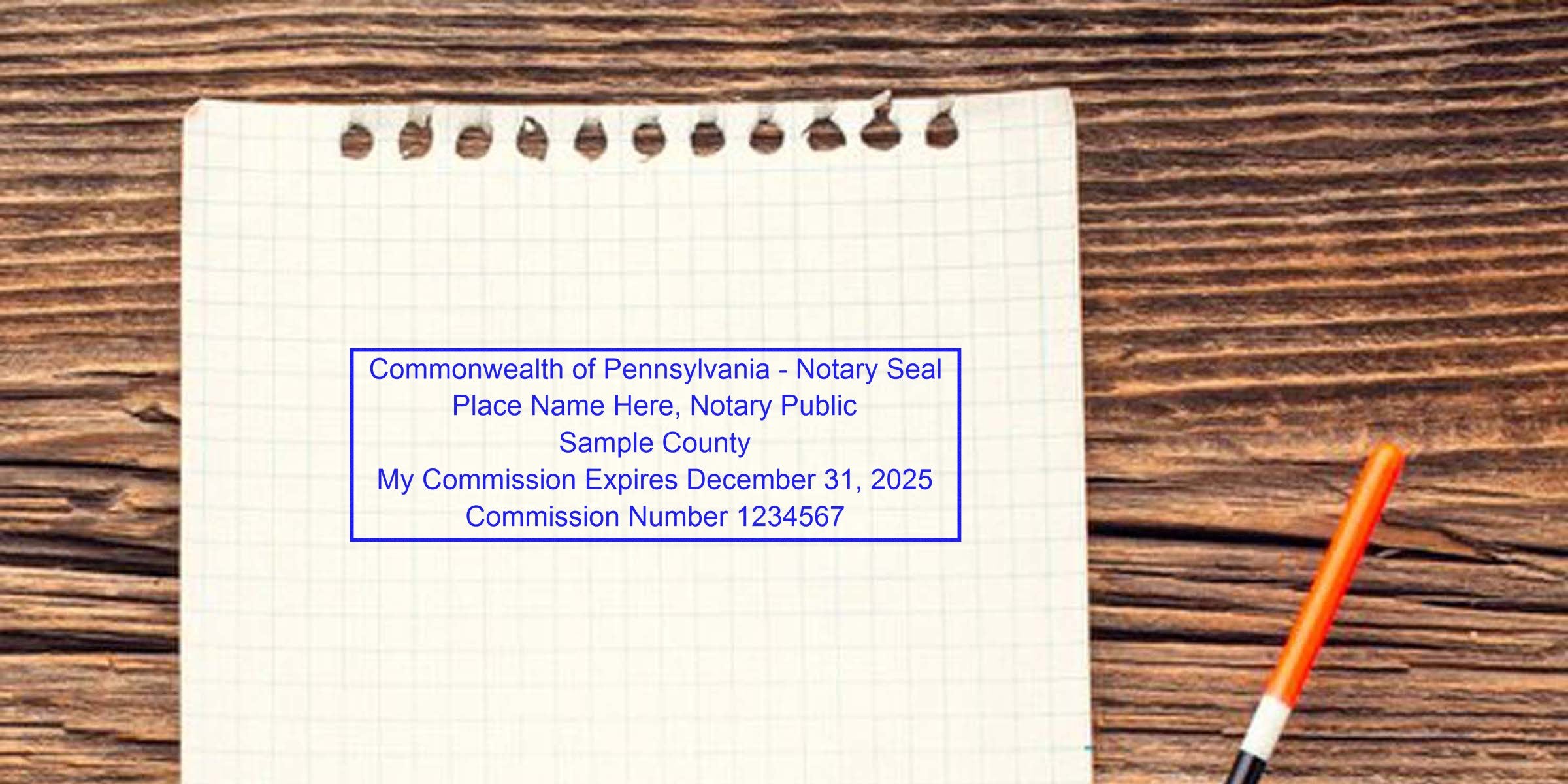 Top-down shot of torn graph paper on a wooden desk showing a blue Commonwealth of Pennsylvania notary seal sample and an orange pen at right, suitable for notary, legal, office, or stationery visuals.