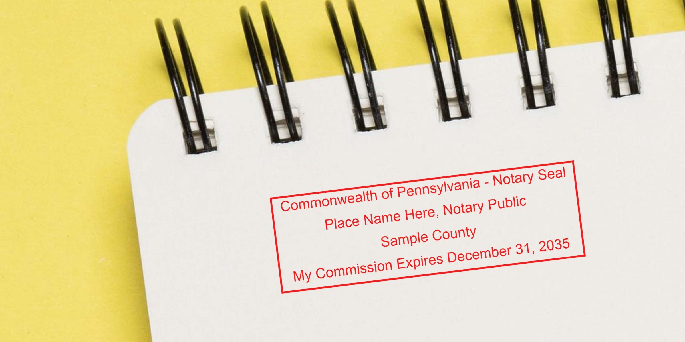 Close-up of a spiral-bound white notebook page on yellow background with a red Commonwealth of Pennsylvania notary seal sample stamp reading "Place Name Here, Notary Public" and commission expiration date placeholder.