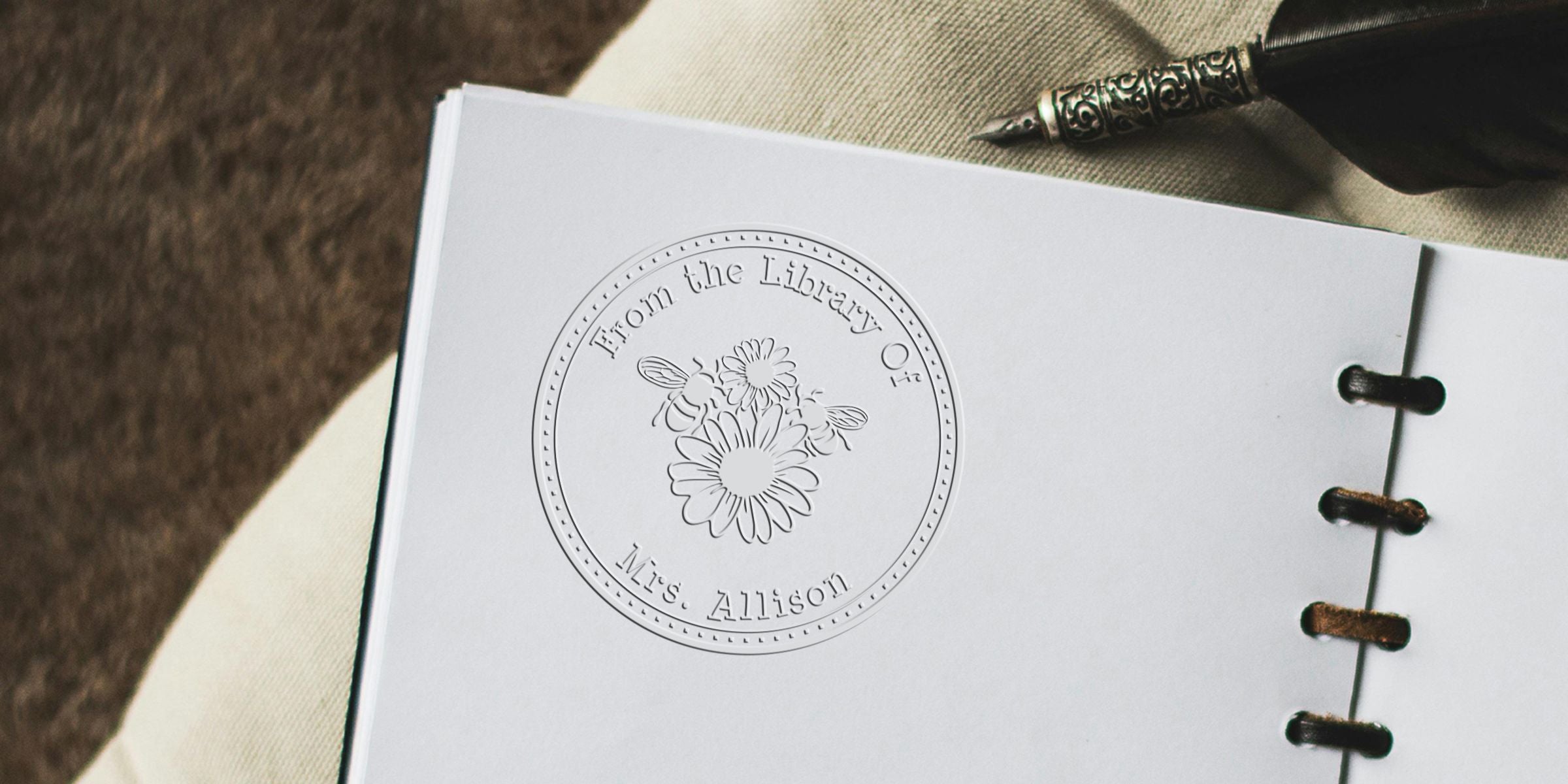Circular stamp on a page reading “From the Library Of Mrs. Allison” with a bouquet of daisies, in a notebook.