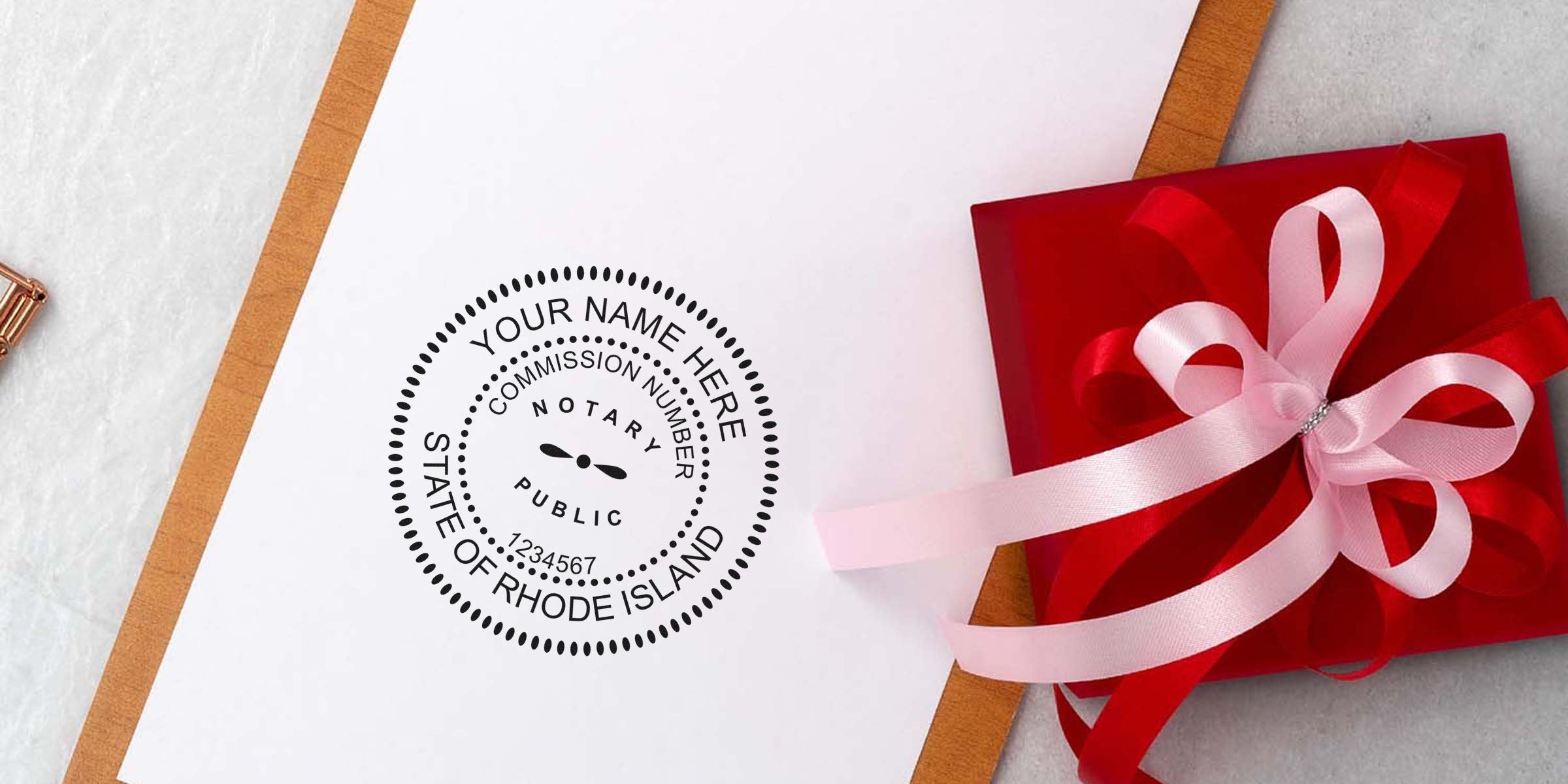 Paper clipboard showing a customizable Rhode Island notary public seal stamp on white paper beside a red gift box with pink ribbon bow