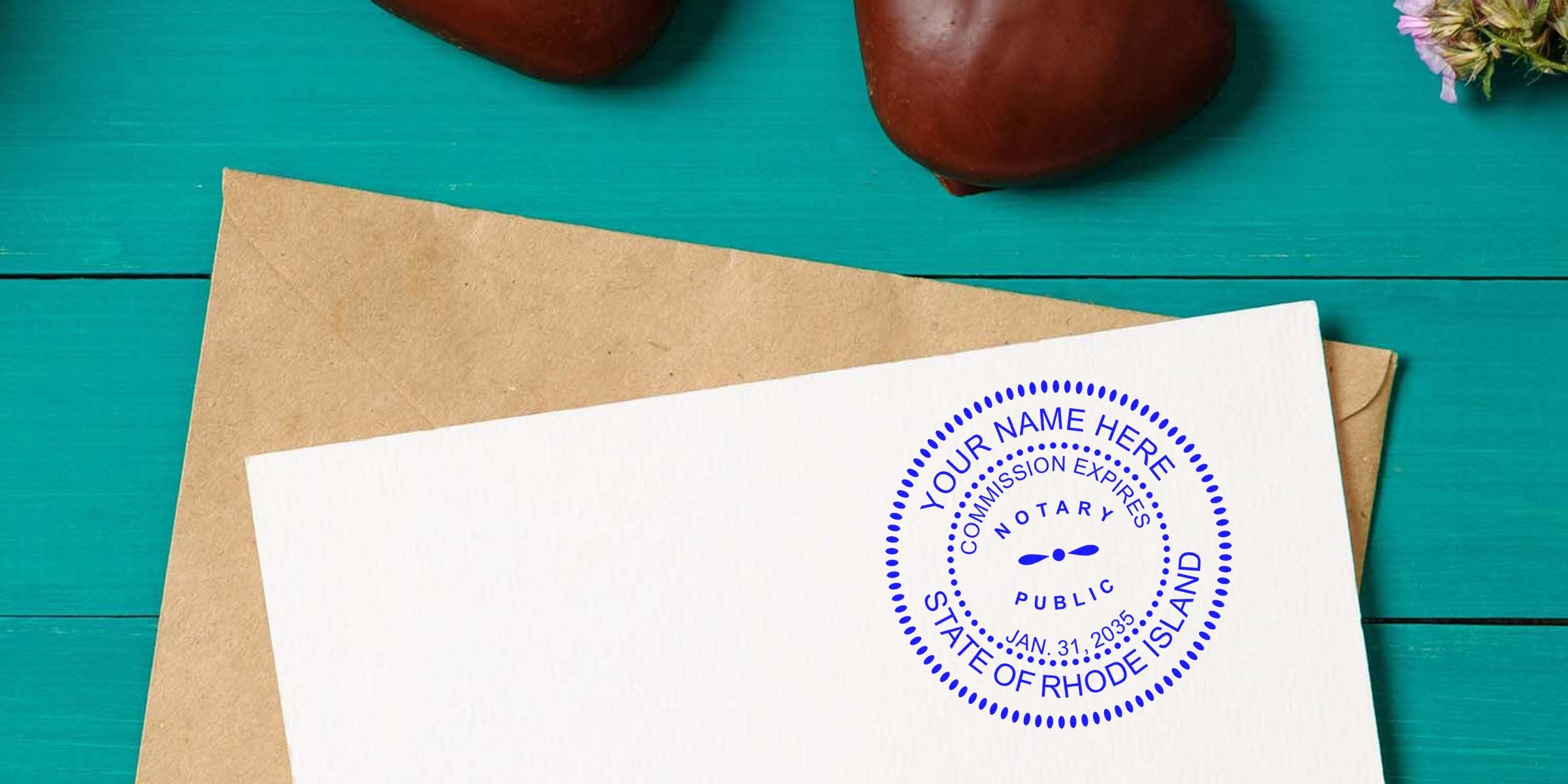 Blue circular notary public stamp reading "State of Rhode Island" on a white card angled over a kraft envelope, set on a teal wooden table with chocolate hearts and small dried flowers visible