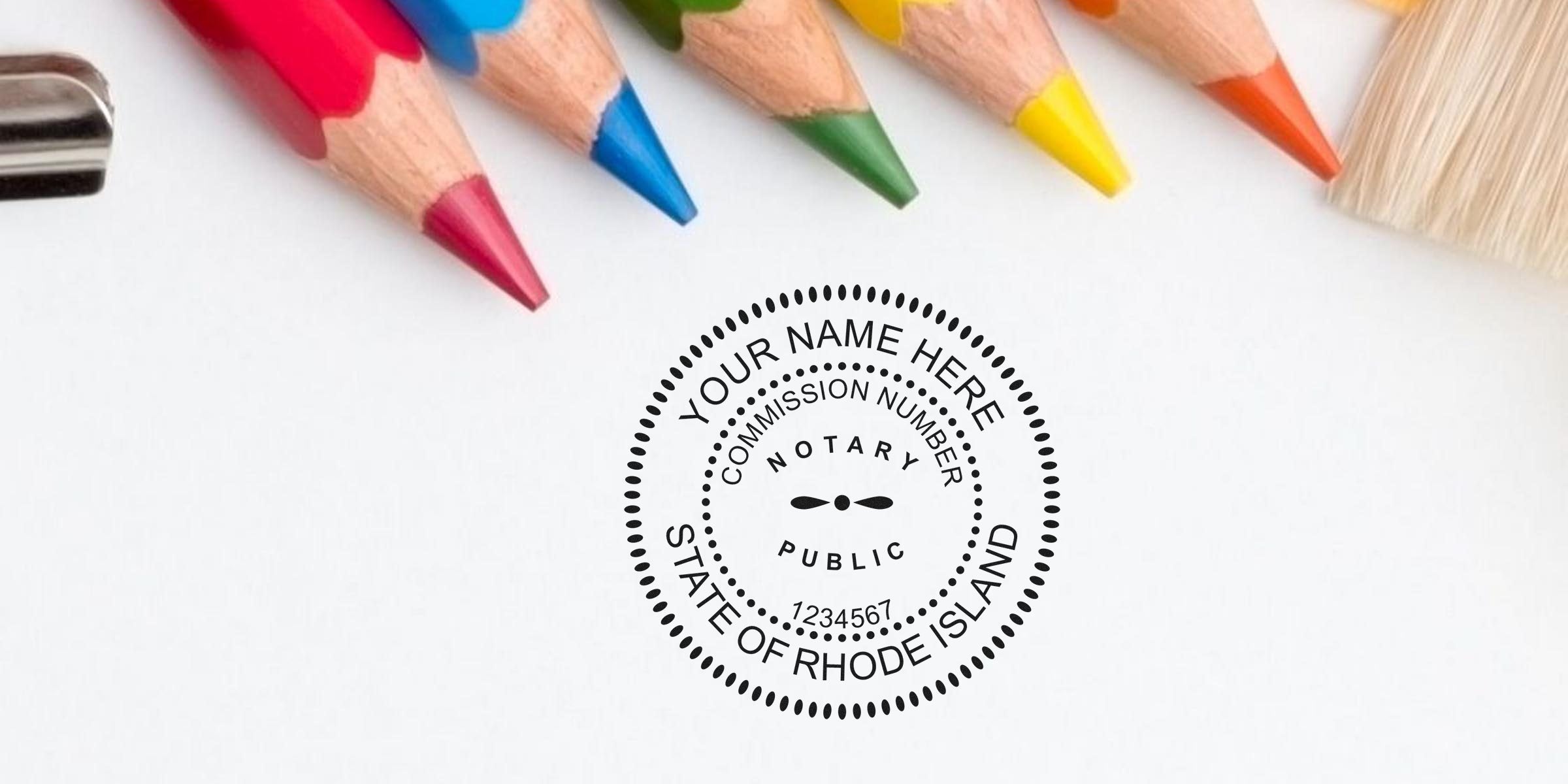 Close-up colored pencils and paintbrush arranged above a blank white sheet featuring a circular notary public stamp mockup reading "Your Name Here, Commission Number, State of Rhode Island."