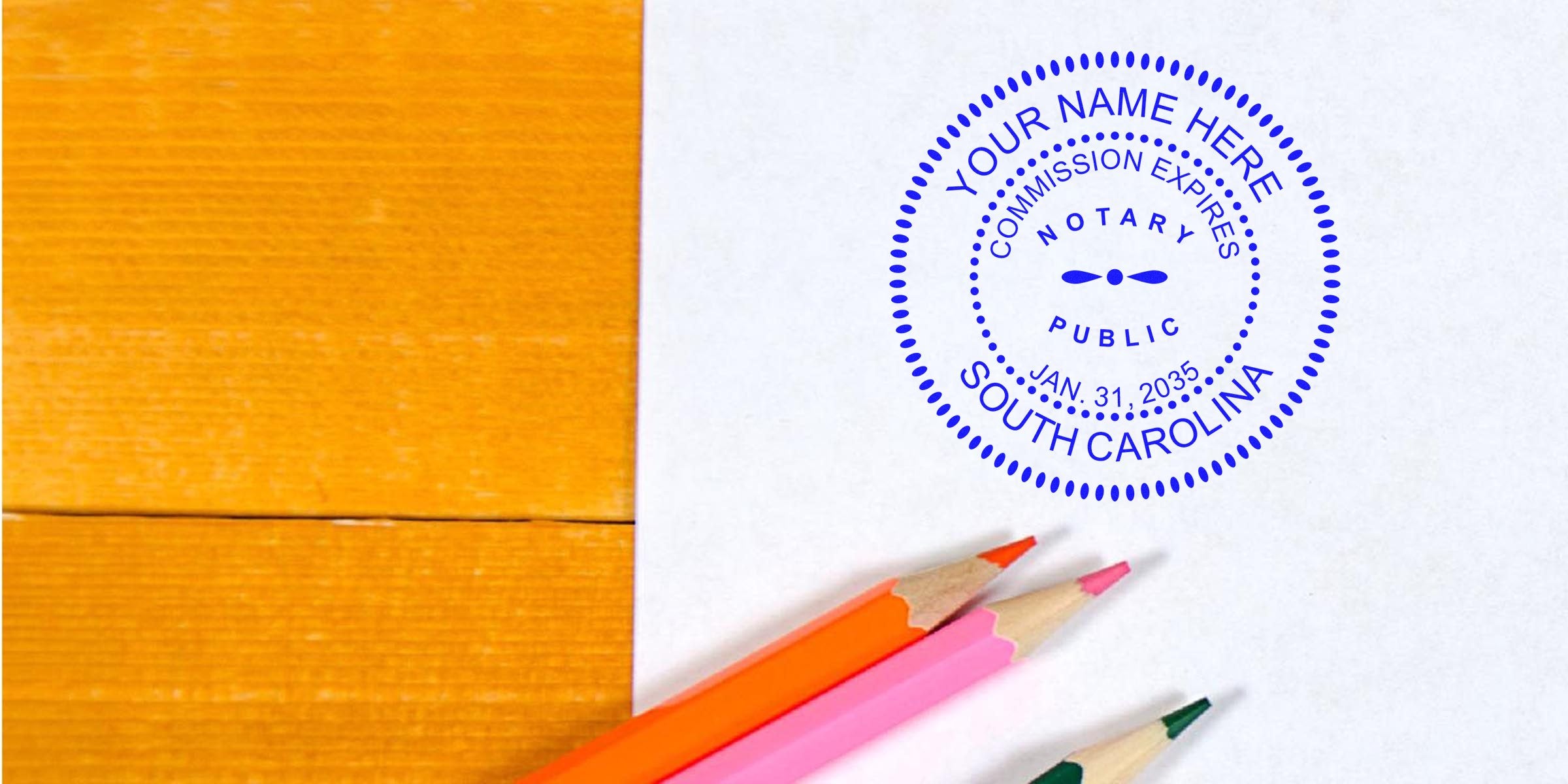 Notary public rubber stamp imprint reading "Your Name Here, South Carolina" on white paper beside orange wood surface and three colored pencils (orange, pink, green) — business notarization concept, mockup for notary services.
