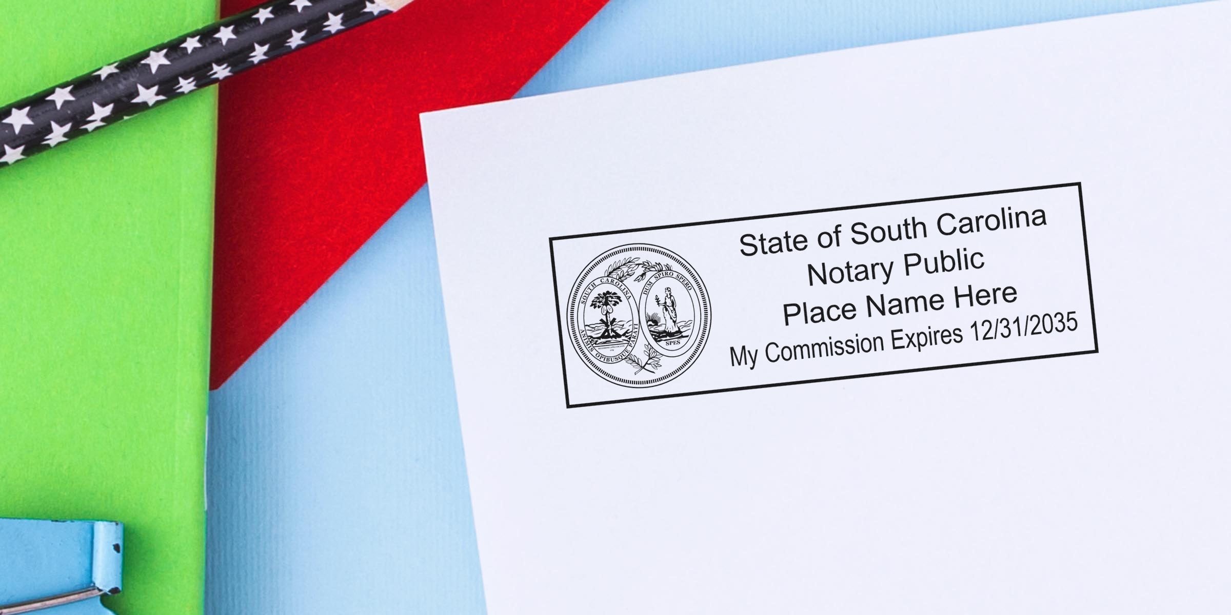 Close-up of State of South Carolina notary public stamp on white paper reading "Place Name Here" with commission expires 12/31/2035, photographed on colorful green, red and blue background with star-pattern pencil.