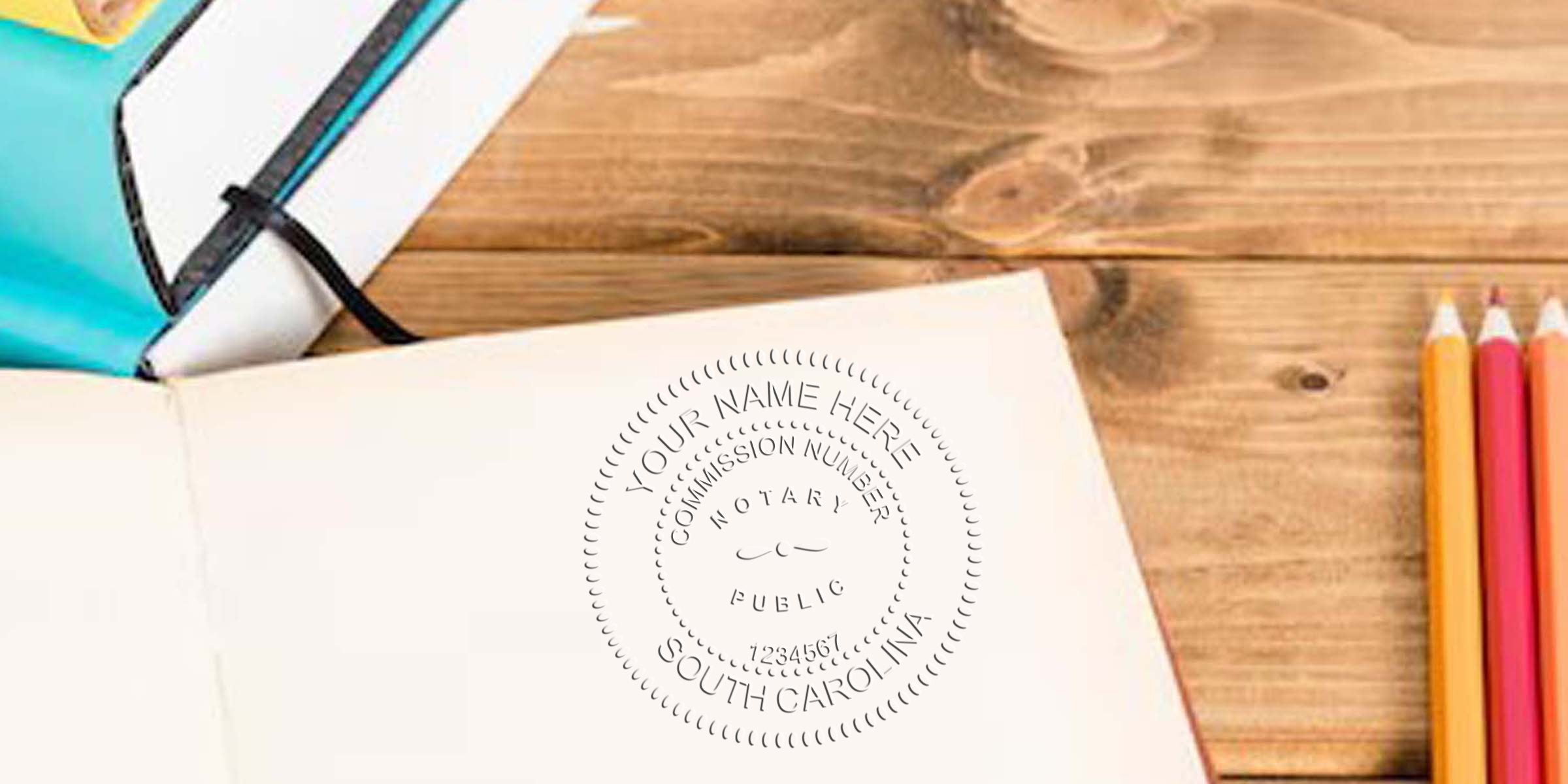 Open notebook on a wooden desk with an embossed notary public seal reading "Your Name Here, South Carolina" stamped on the page; colored pencils and a closed teal notebook nearby — notary, legal document, stationery.