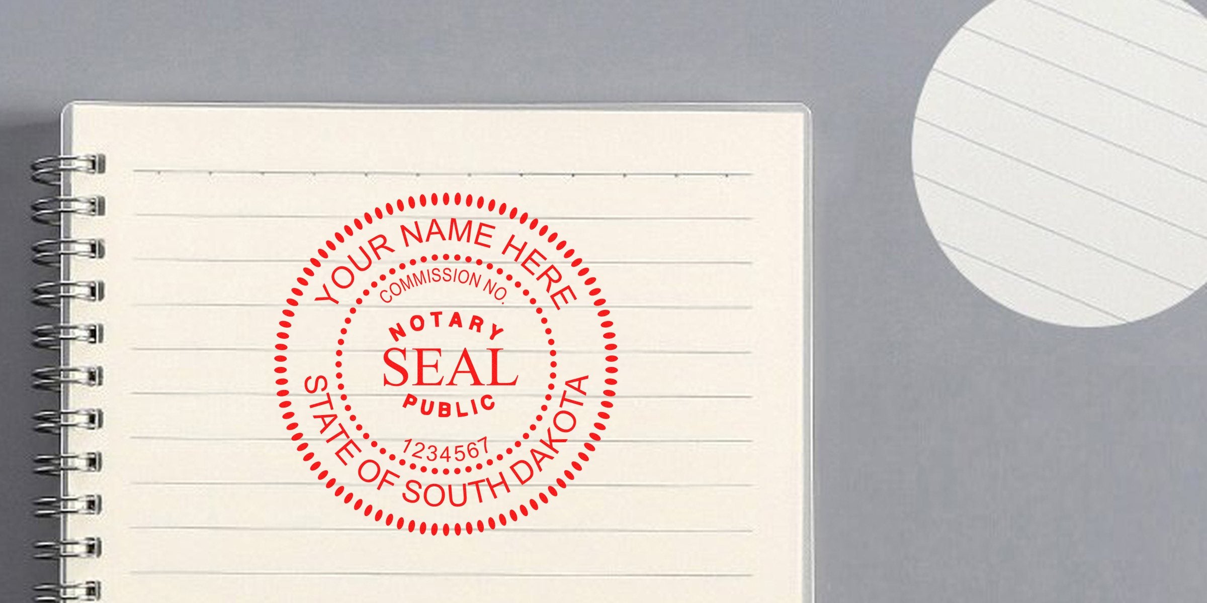 Red circular notary seal stamp reading "Notary Seal Public" with placeholder "Your Name Here, State of South Dakota" printed on an open lined spiral notebook against a gray background