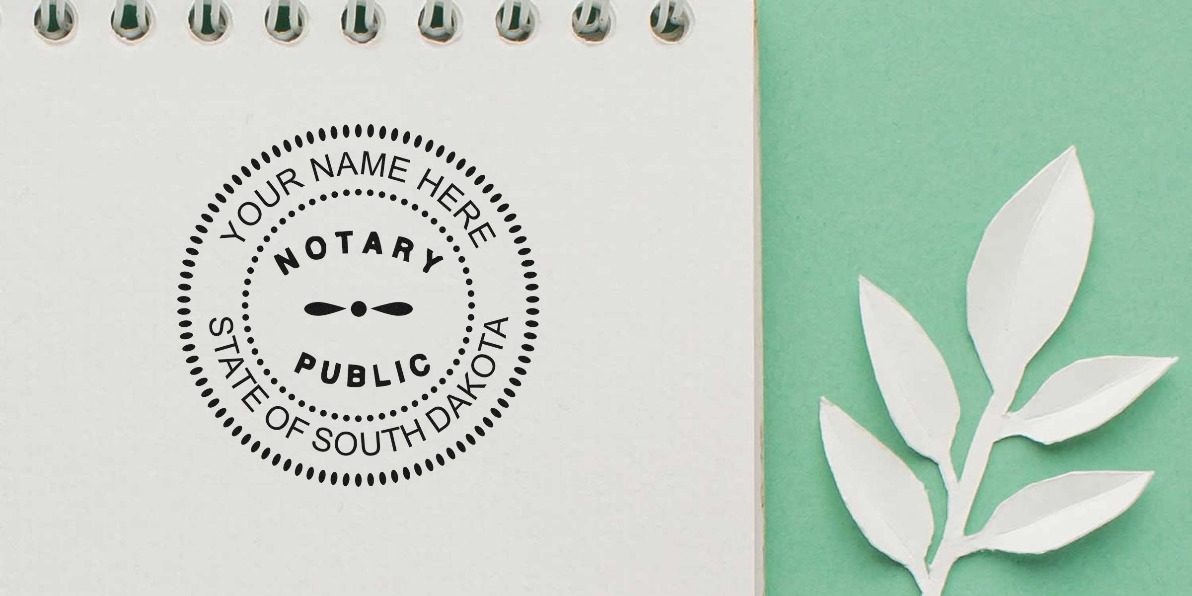 Spiral notebook page with a black circular "Notary Public" stamp reading "Your Name Here, State of South Dakota" beside a white paper leaf on a mint green background