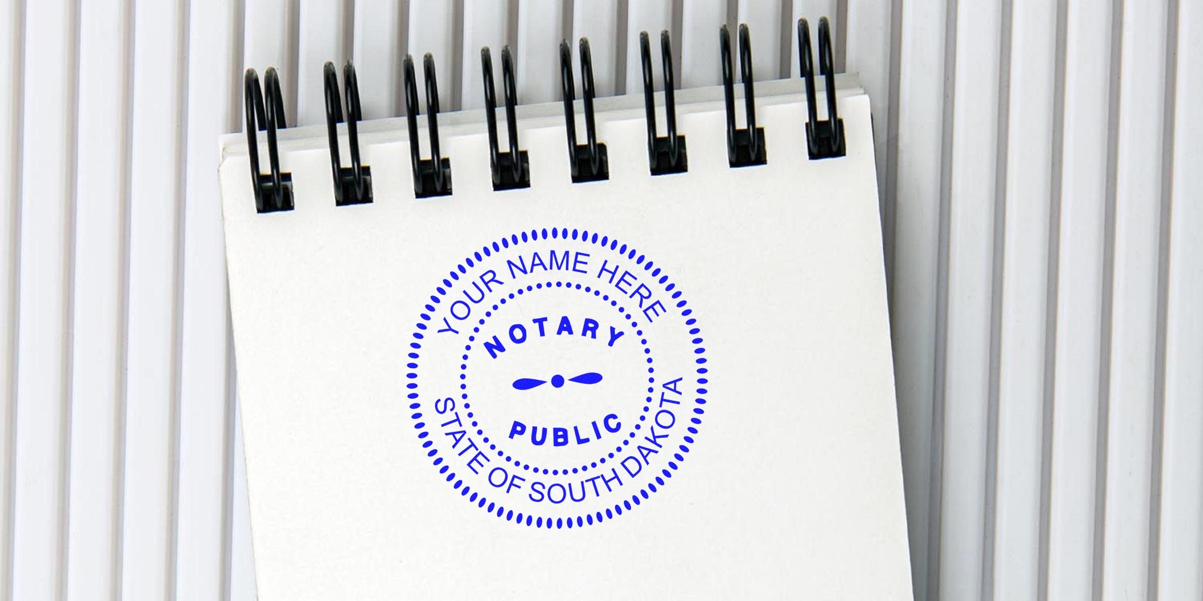 Spiral-bound white notepad with a blue circular "Notary Public" stamp mockup reading "Your Name Here, State of South Dakota" against a ribbed white background