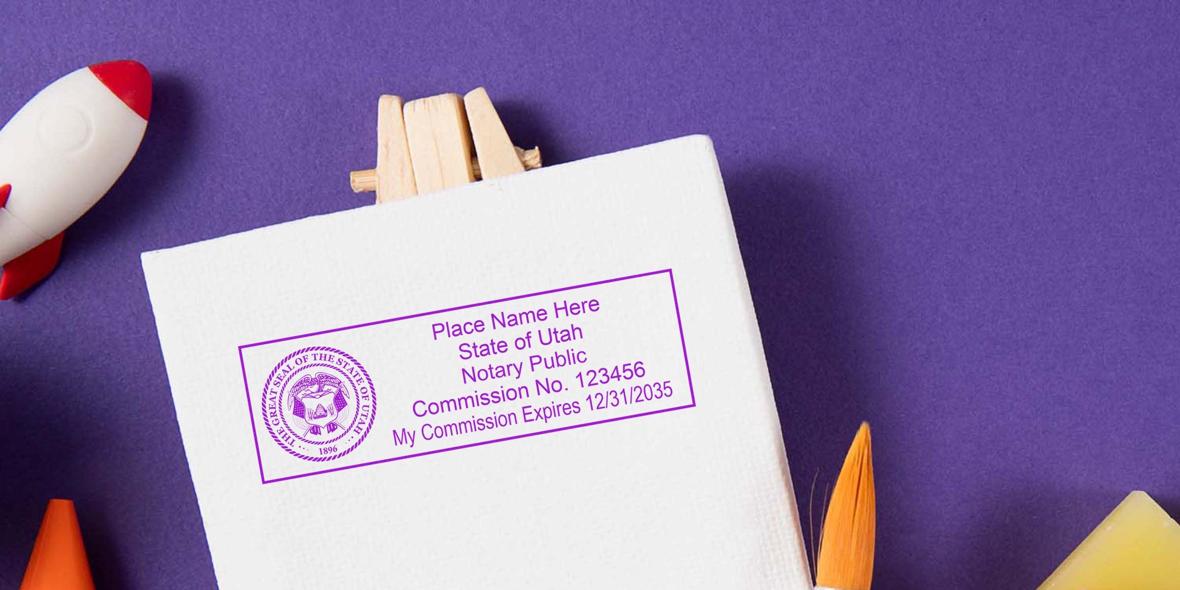 Purple notary stamp imprint mockup on white canvas reading "State of Utah Notary Public" with commission number, set on purple background alongside a toy rocket and paintbrush—stationery branding and notary service concept.