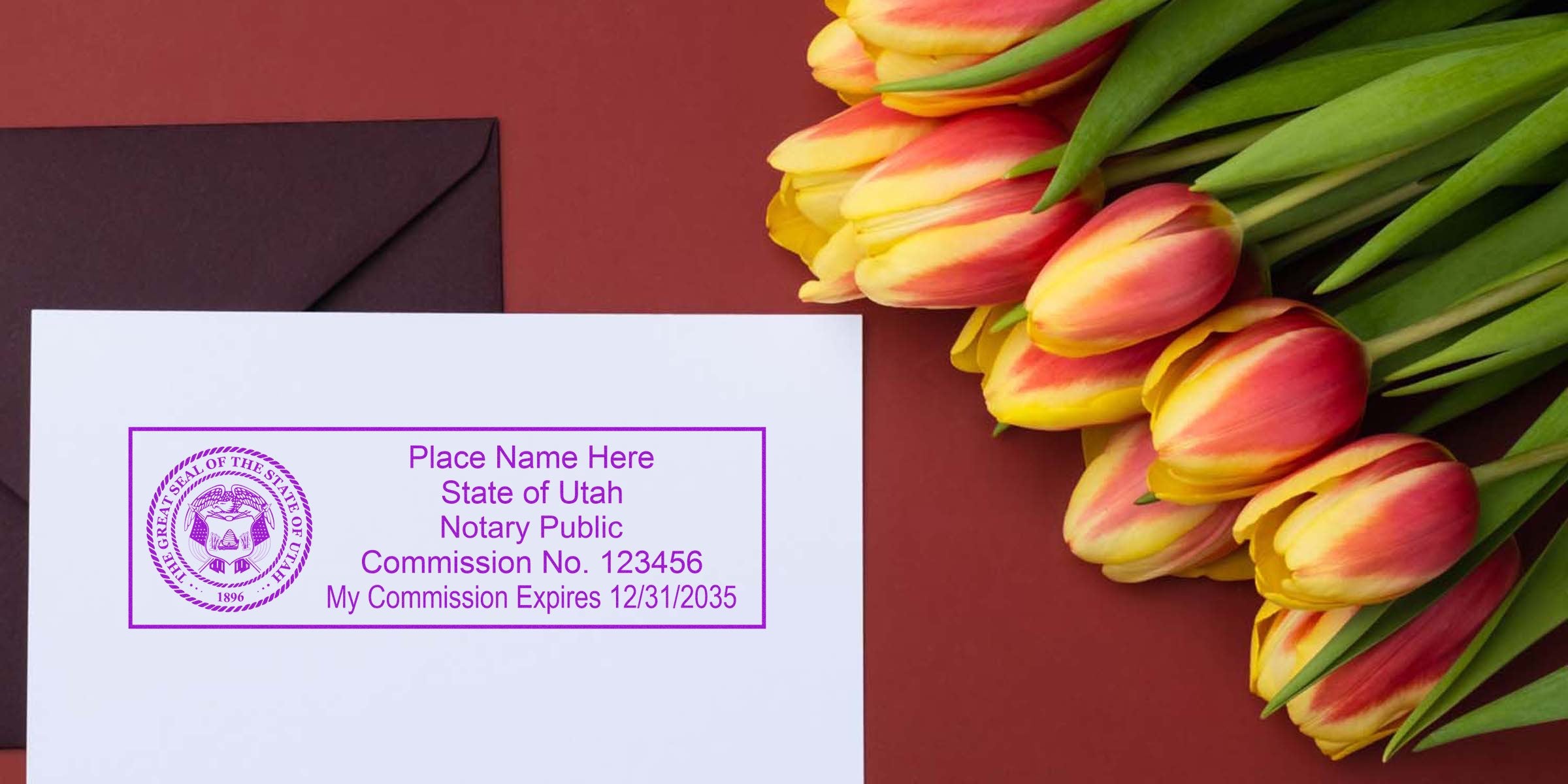 Flat lay of a purple Utah notary public stamp on white paper beside a dark brown envelope and a bouquet of red-yellow tulips on a maroon background