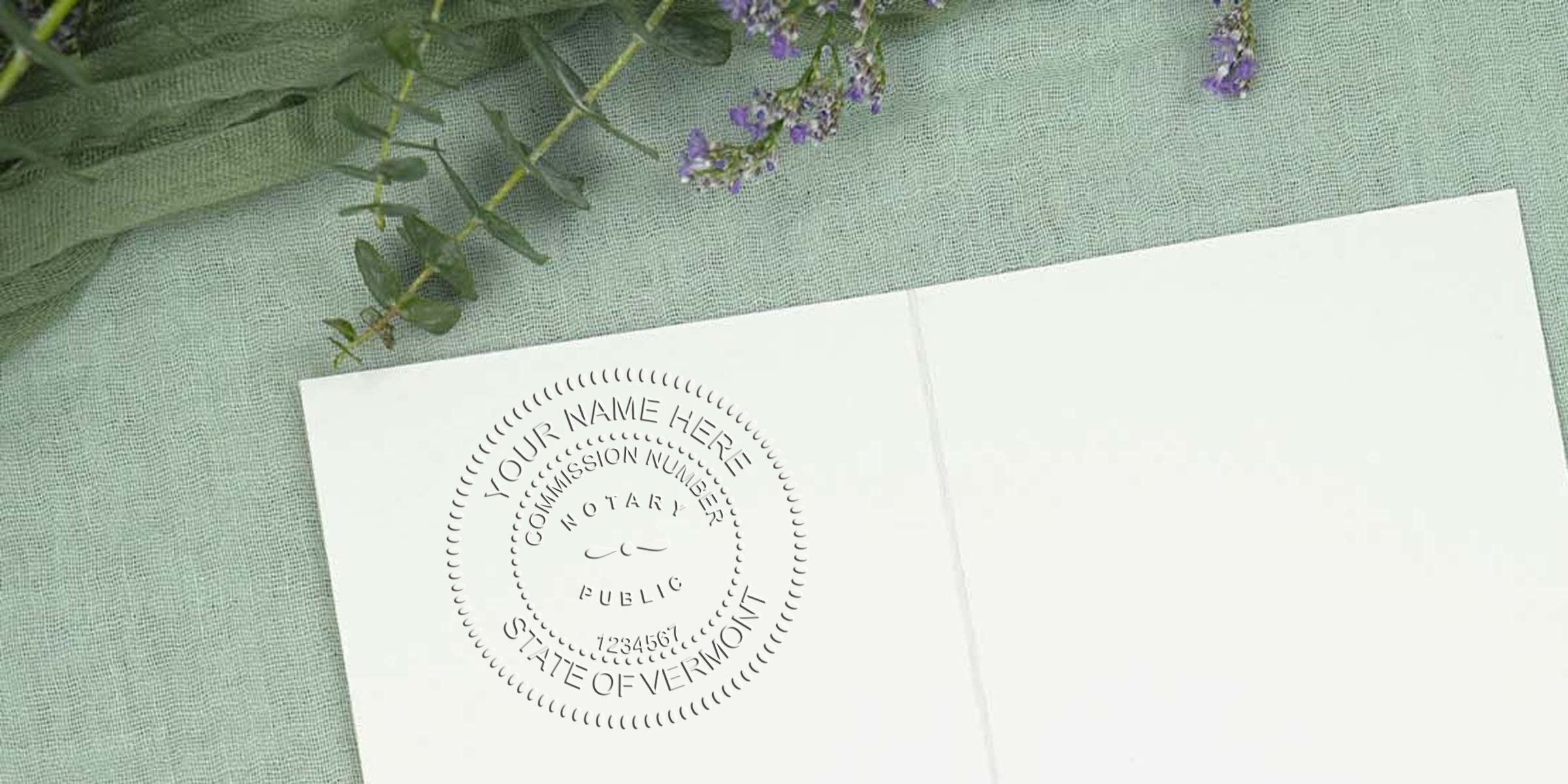 Embossed notary seal impression on a white card with "State of Vermont" visible, set on mint linen fabric with eucalyptus and small purple flowers