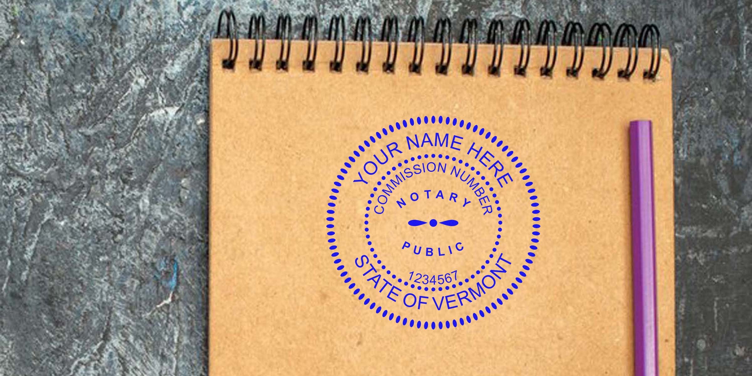 Top-down photo of a brown spiral notebook with a blue circular Vermont notary public stamp mockup reading "Your Name Here, Commission Number, State of Vermont" and a purple pen on a dark textured surface