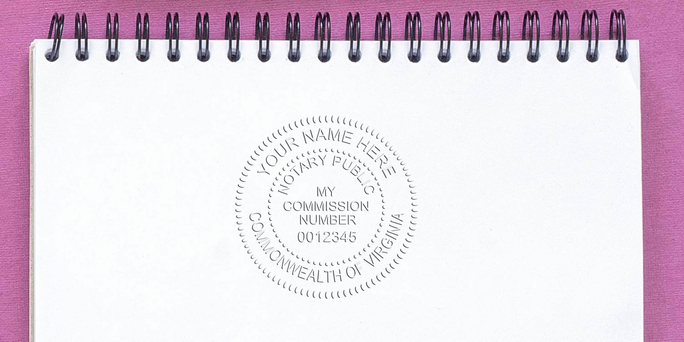 Spiral-bound notebook with embossed notary public seal reading "Your Name Here, Notary Public, My Commission Number 0012345, Commonwealth of Virginia" on a blank white page against a pink background