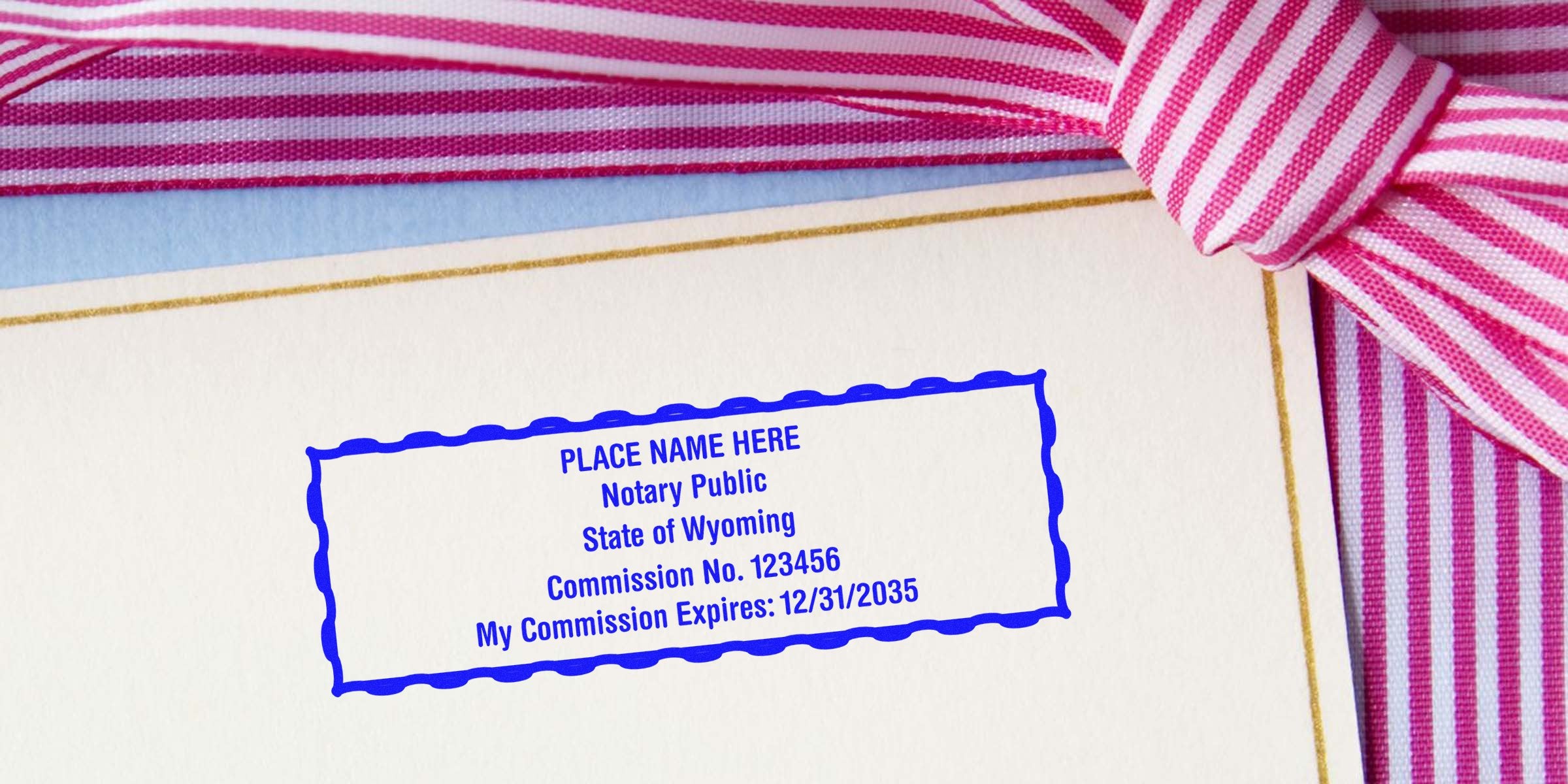 Blue notary public stamp sample reading "Place Name Here, Notary Public, State of Wyoming, Commission No. 123456, My Commission Expires: 12/31/2035" on cream card with gold trim and pink striped ribbon bow.