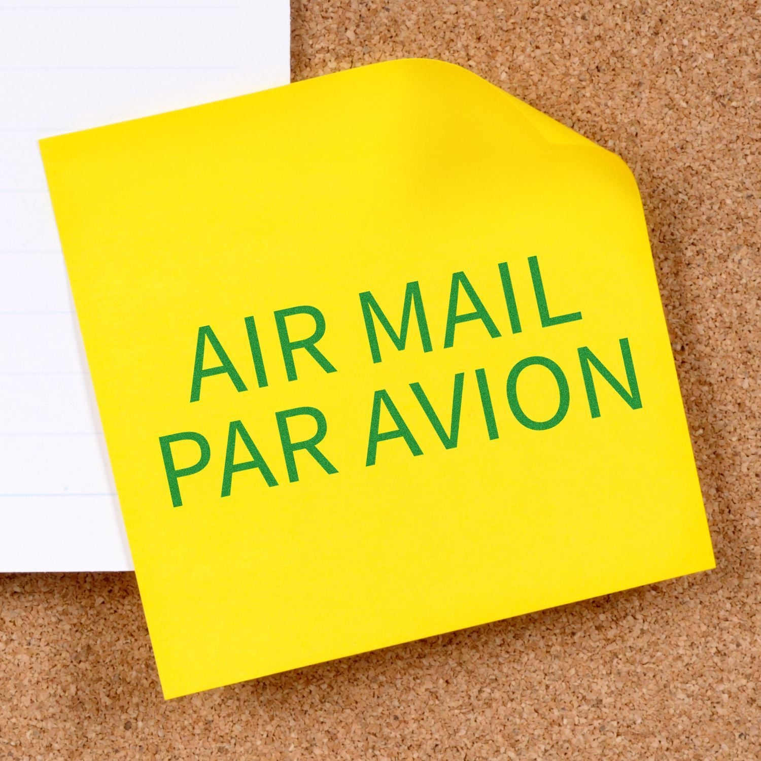 Postal and Mailing Rubber Stamps Blog Post Feature Image: Yellow sticky note with 'AIR MAIL PAR AVION' text on a corkboard.