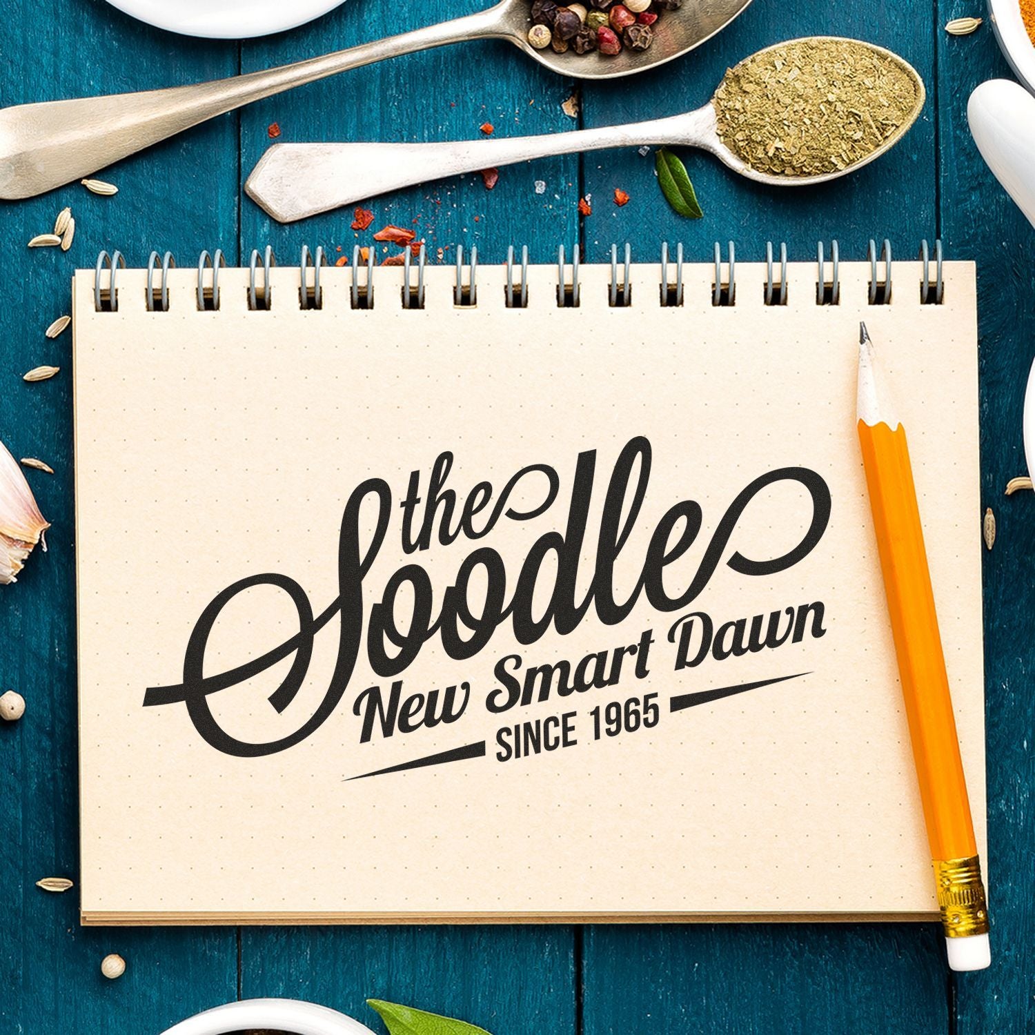 A notebook with the Soodle New Smart Dawn Since 1965 written on it, surrounded by spices and a pencil. Blog post: Create Your Own Customized Stamp for Business Feature Post Image.