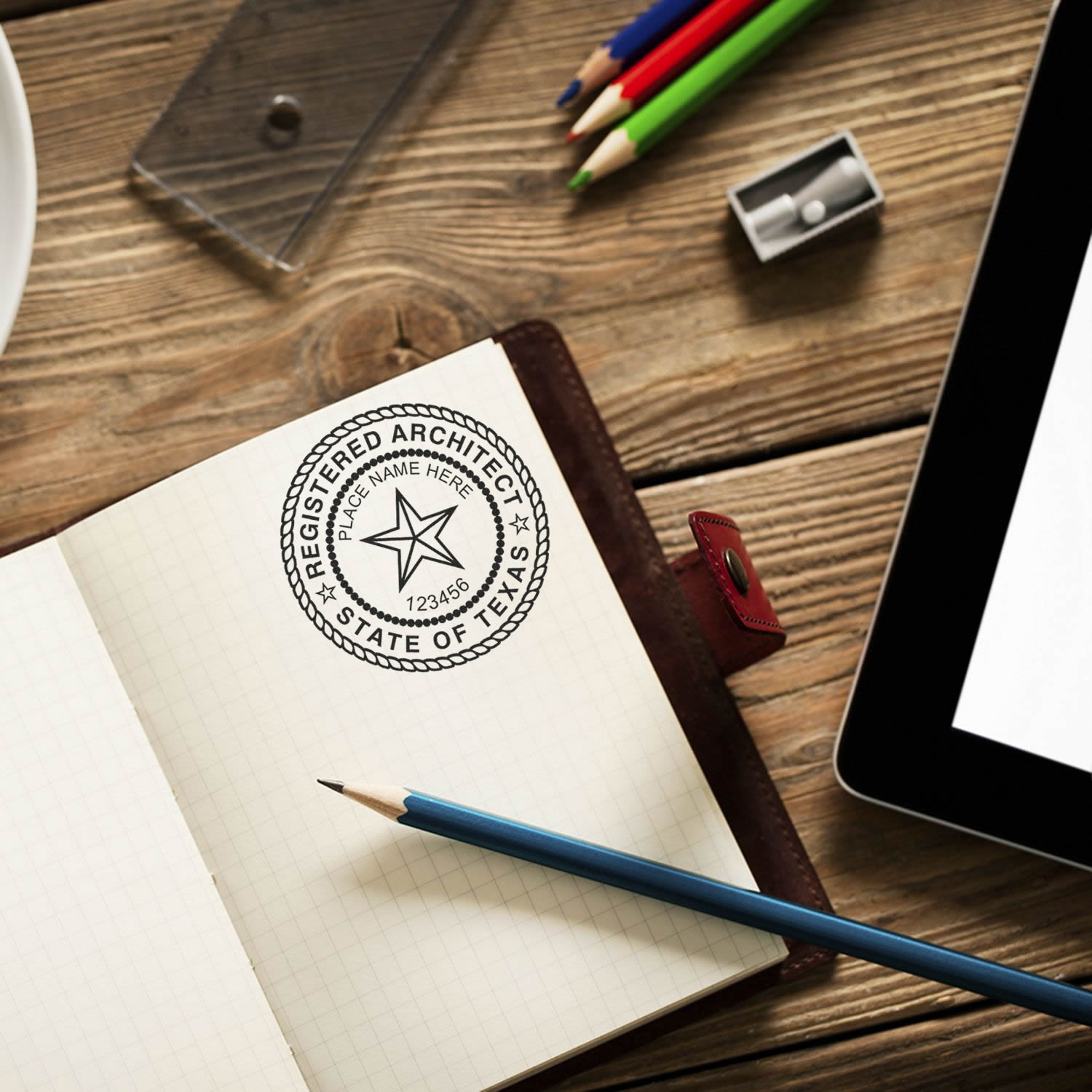 A Texas architect's seal and stamp on a notebook, surrounded by pencils and a tablet. Blog post: Texas Architectural Seals and Stamps.