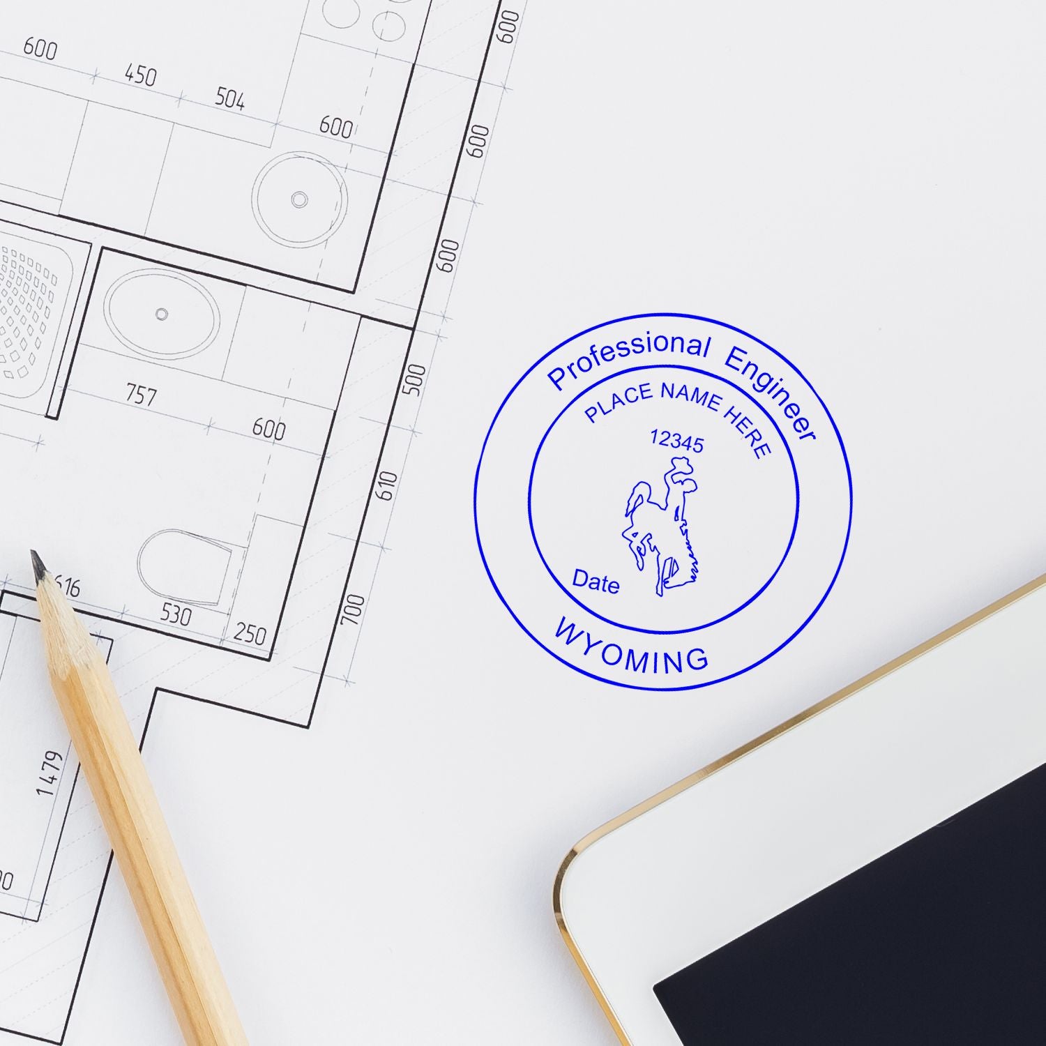 A Wyoming PE Embosser stamp on an engineering blueprint with a pencil and a tablet nearby. Blog post: Wyoming PE Embossers.