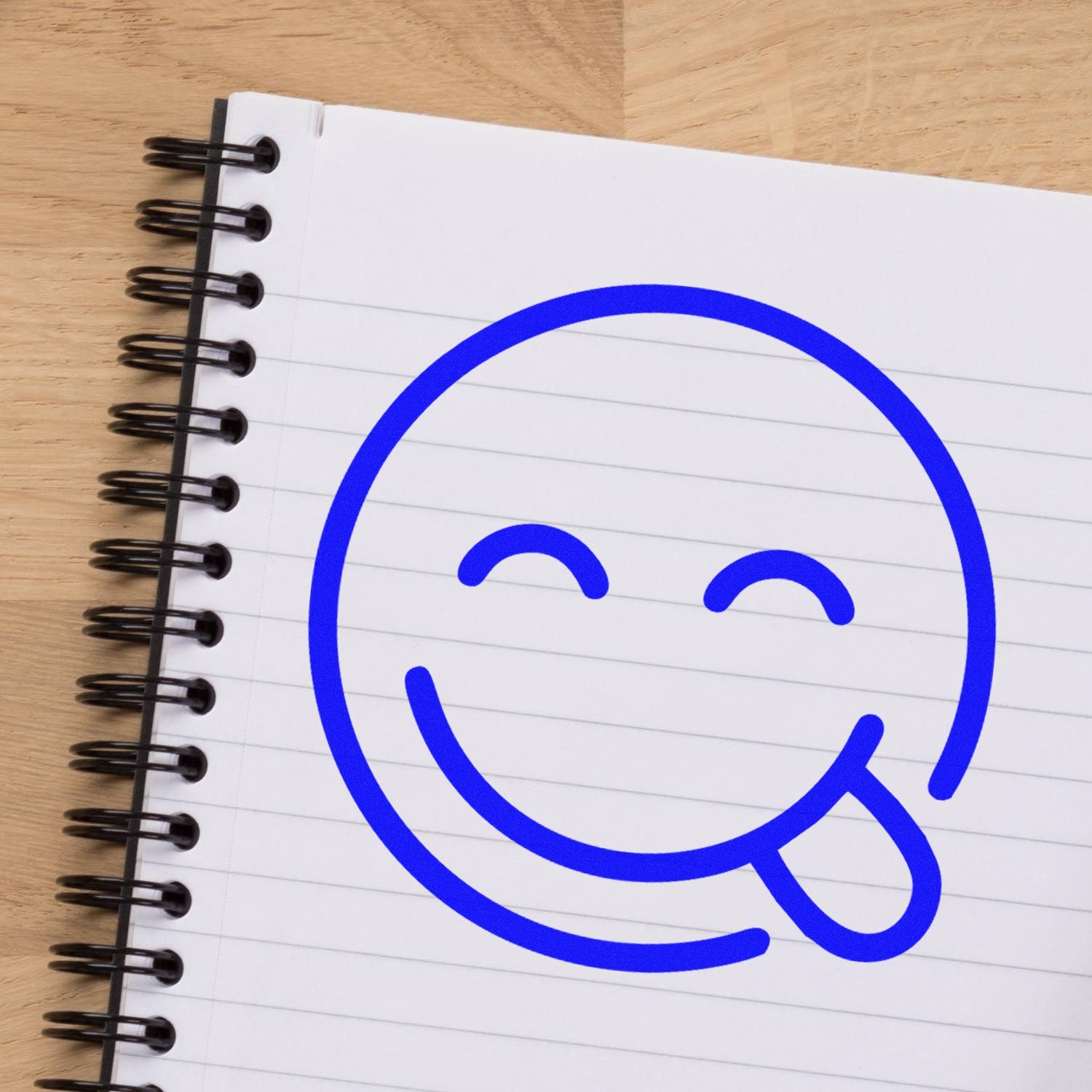 Wood Handle Silly Smirk Pictogram Rubber Stamp imprint on notebook, featuring a playful blue smirk face with tongue out. Ideal for adding fun to stationery and crafts.