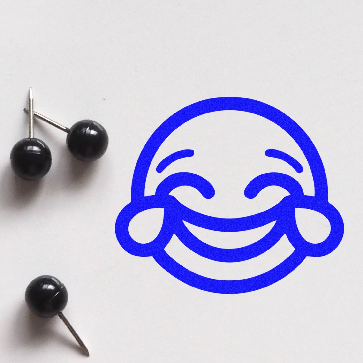 Wood Handle Cheeky Grin Emoji Rubber Stamp on white paper, showcasing a bold blue cheeky grin emoji design. Perfect for adding a playful touch to crafts and stationery.