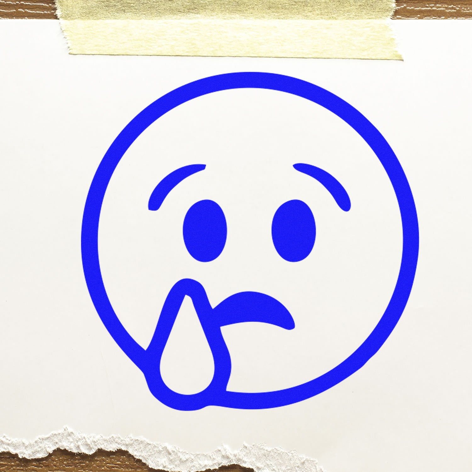 Image of the Wood Handle Sorrowful Droop Smiley Rubber Stamp, featuring a blue sad face with a tear, on white paper. Perfect for adding a touch of emotion to your crafts and stationery.