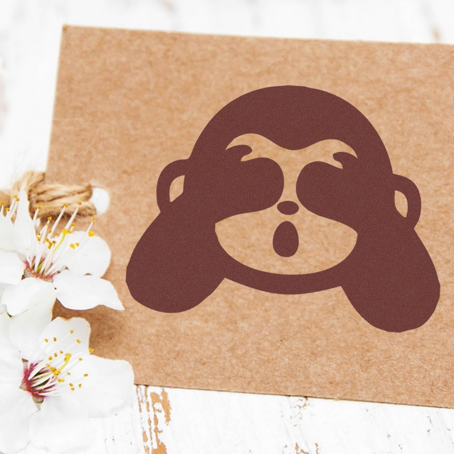 Image of a Self-Inking Blindfolded Monkey Emojicons Stamp on a brown card, featuring a playful monkey face with hands over eyes. Perfect for adding fun, expressive touches to crafts and letters.