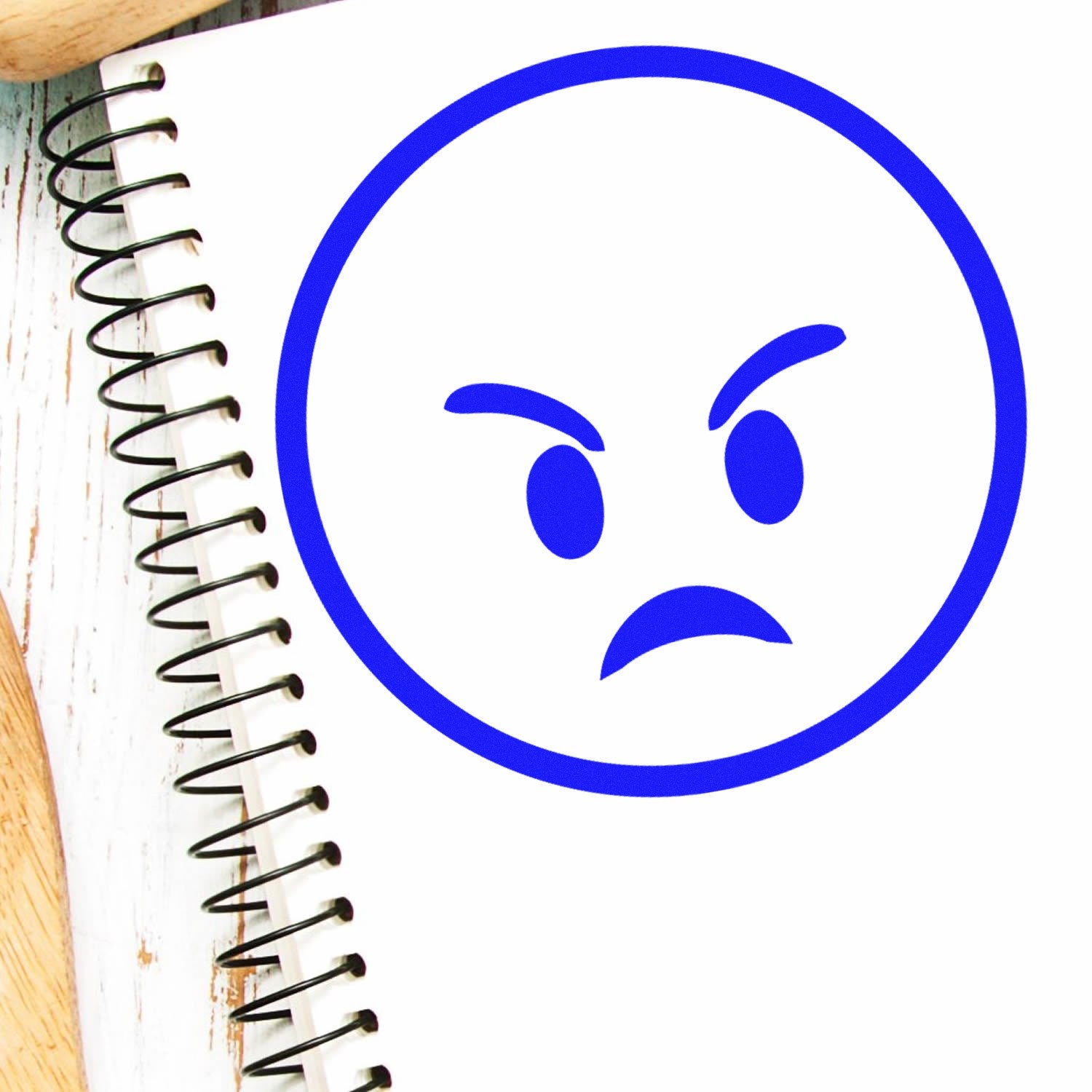 Self-Inking Furious Fred Emoji Stamp on a spiral notebook, featuring a bold blue angry face design. Perfect for adding expressive flair to your notes and documents.