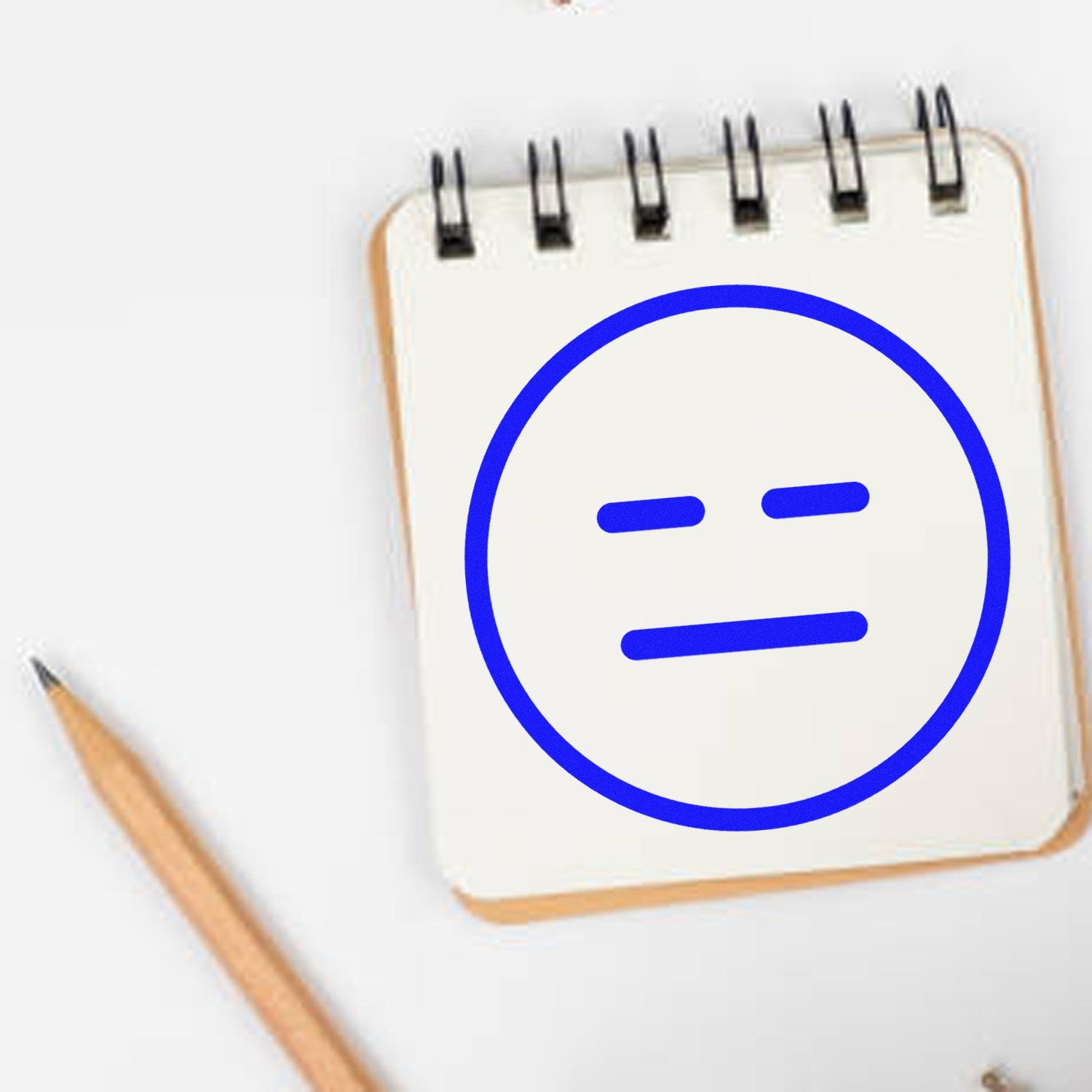 Wood Handle Expressionless Eddie Emoji Rubber Stamp on a notepad, featuring a simple, blue expressionless face. Ideal for adding a unique touch to stationery or crafts.