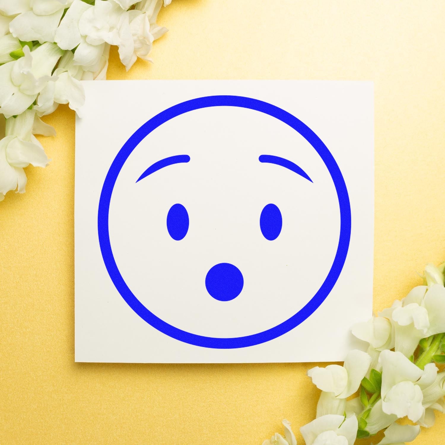 Wood Handle Surprised Stanley Smiley Rubber Stamp with a surprised face design, featuring a wooden handle and blue ink impression on a white card, surrounded by white flowers on a gold background.