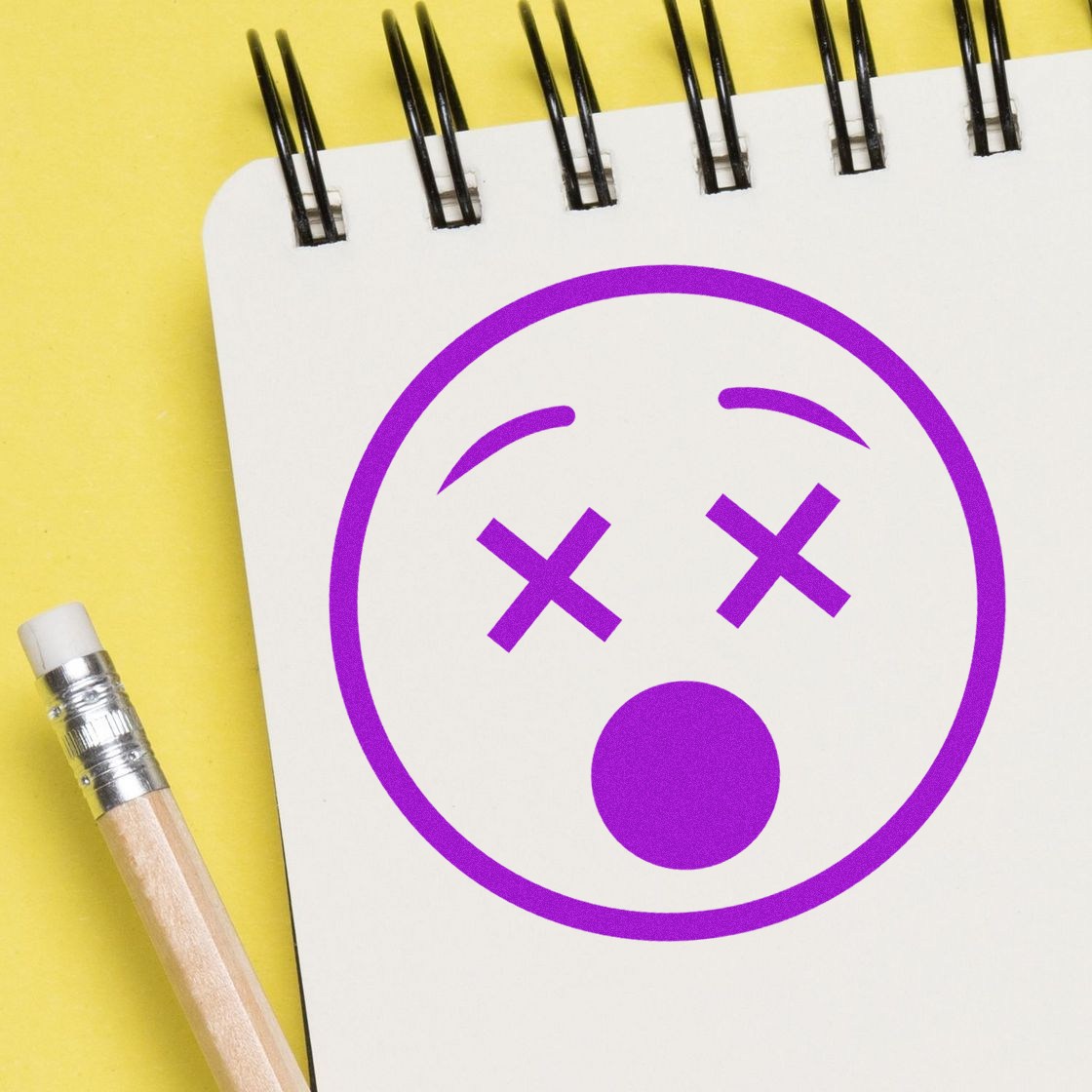 Wood Handle X'd Out Facial Expressions Rubber Stamp on a notepad, featuring a purple face with X eyes and open mouth, next to a pencil. Perfect for creative projects and expressive designs.