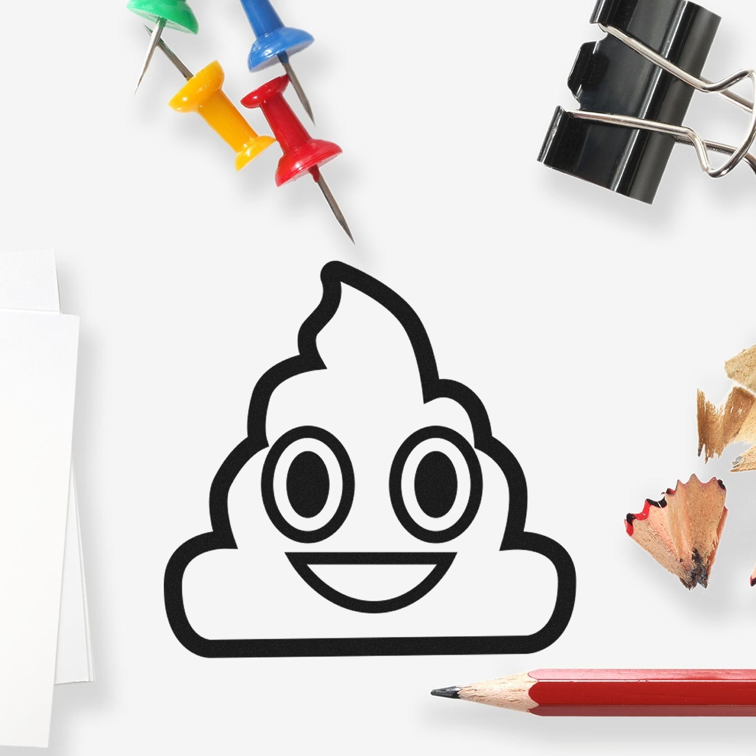 Self-Inking Smiling Poop Emojicons Stamp on a desk with colorful push pins, paper clips, and pencils. Perfect for adding fun to stationery and crafts.