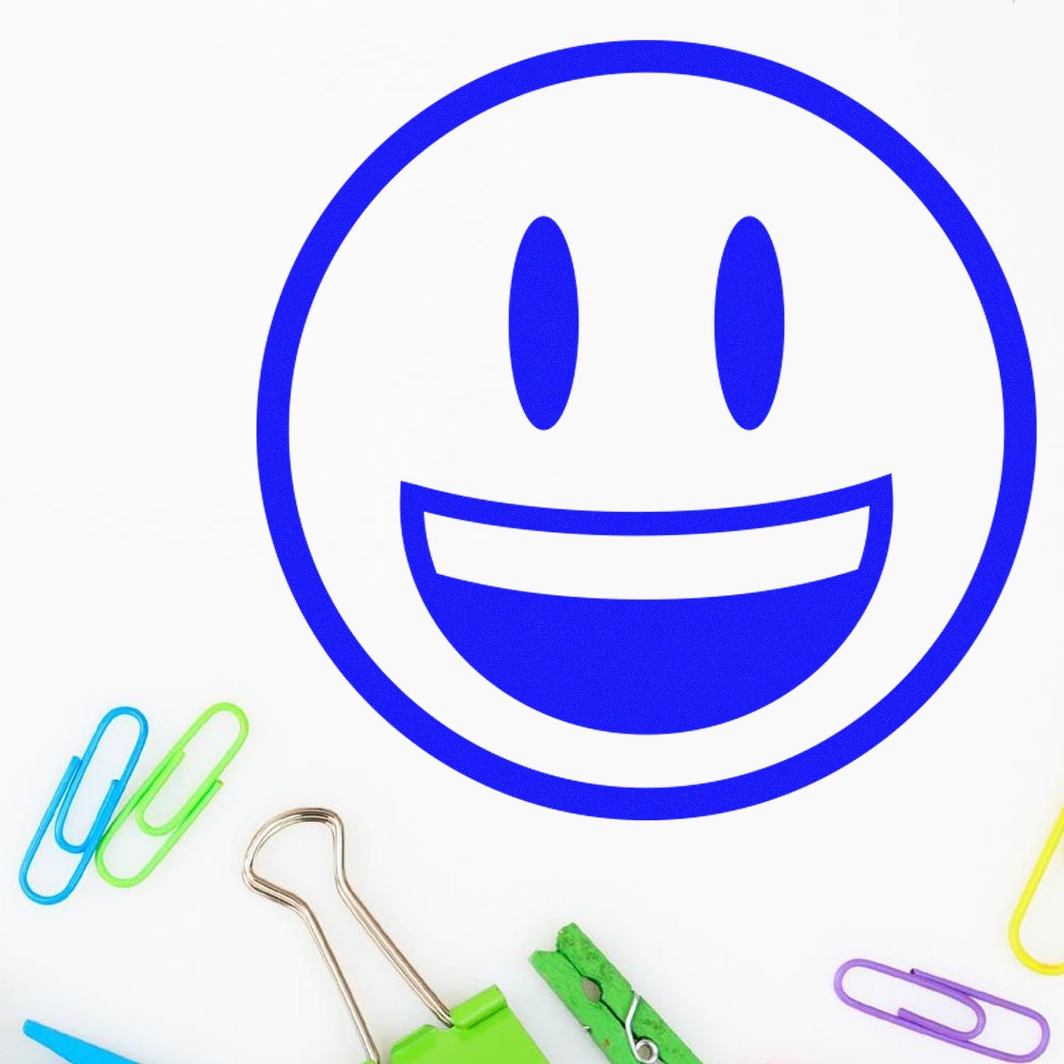 Wood Handle Grinning Delight Emoji Rubber Stamp with a smiling face design, surrounded by colorful paper clips and a binder clip on a white background.