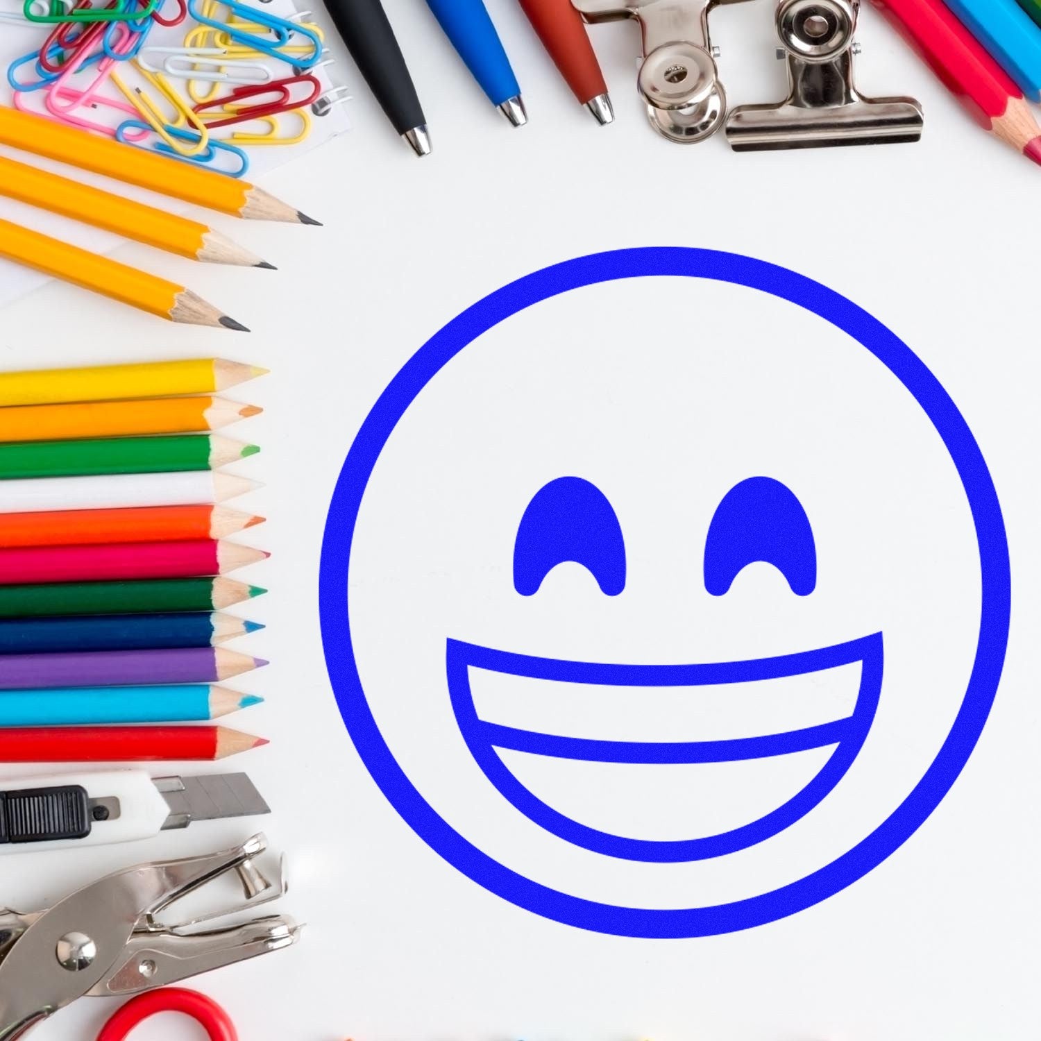 Wood Handle Elated Smile Emoji Rubber Stamp on paper surrounded by colorful pencils, paper clips, and office supplies, showcasing its cheerful design and versatile use.