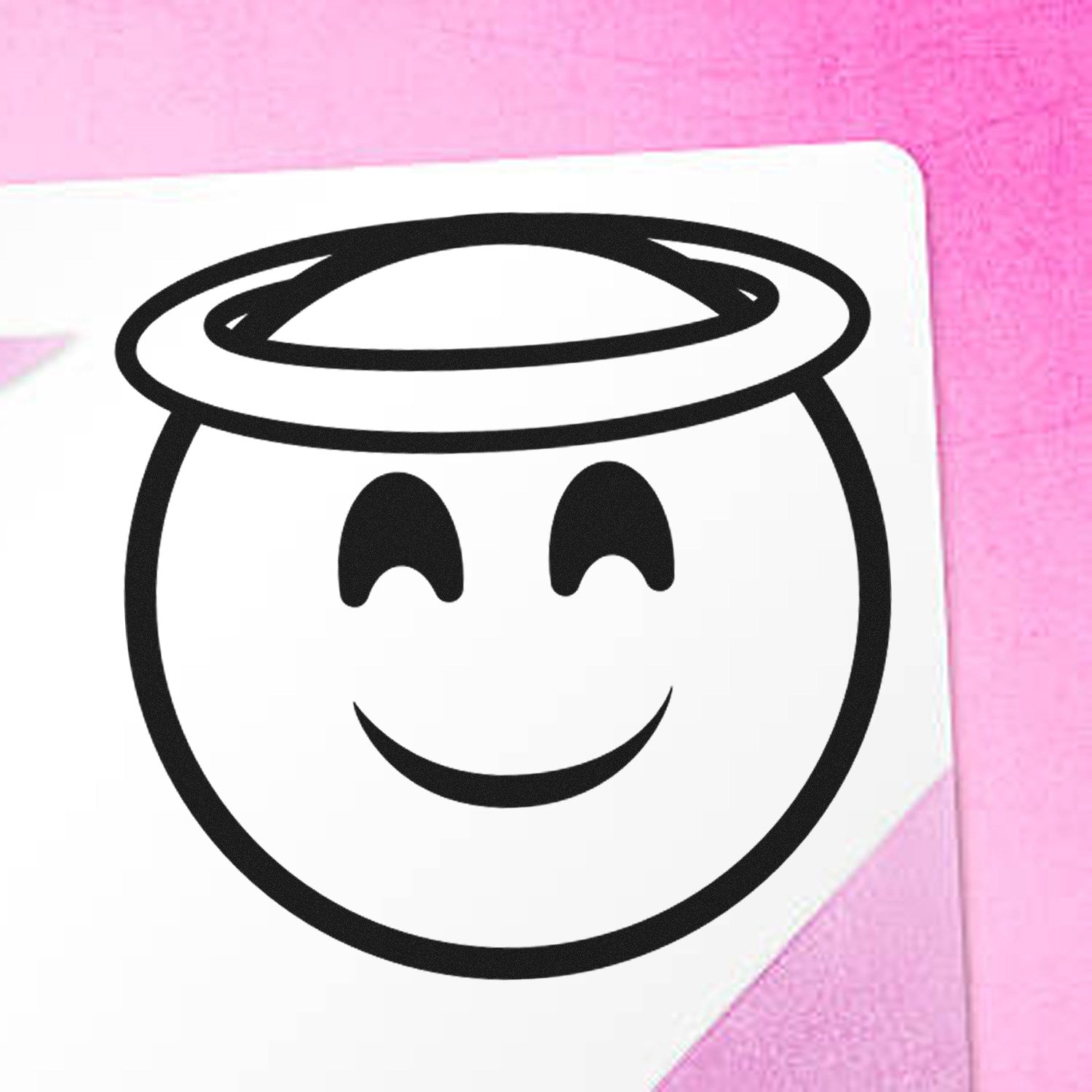 Wood Handle Halo Happiness Emoji Rubber Stamp on pink background, featuring a smiling face with a halo. Perfect for adding a cheerful touch to crafts and stationery.