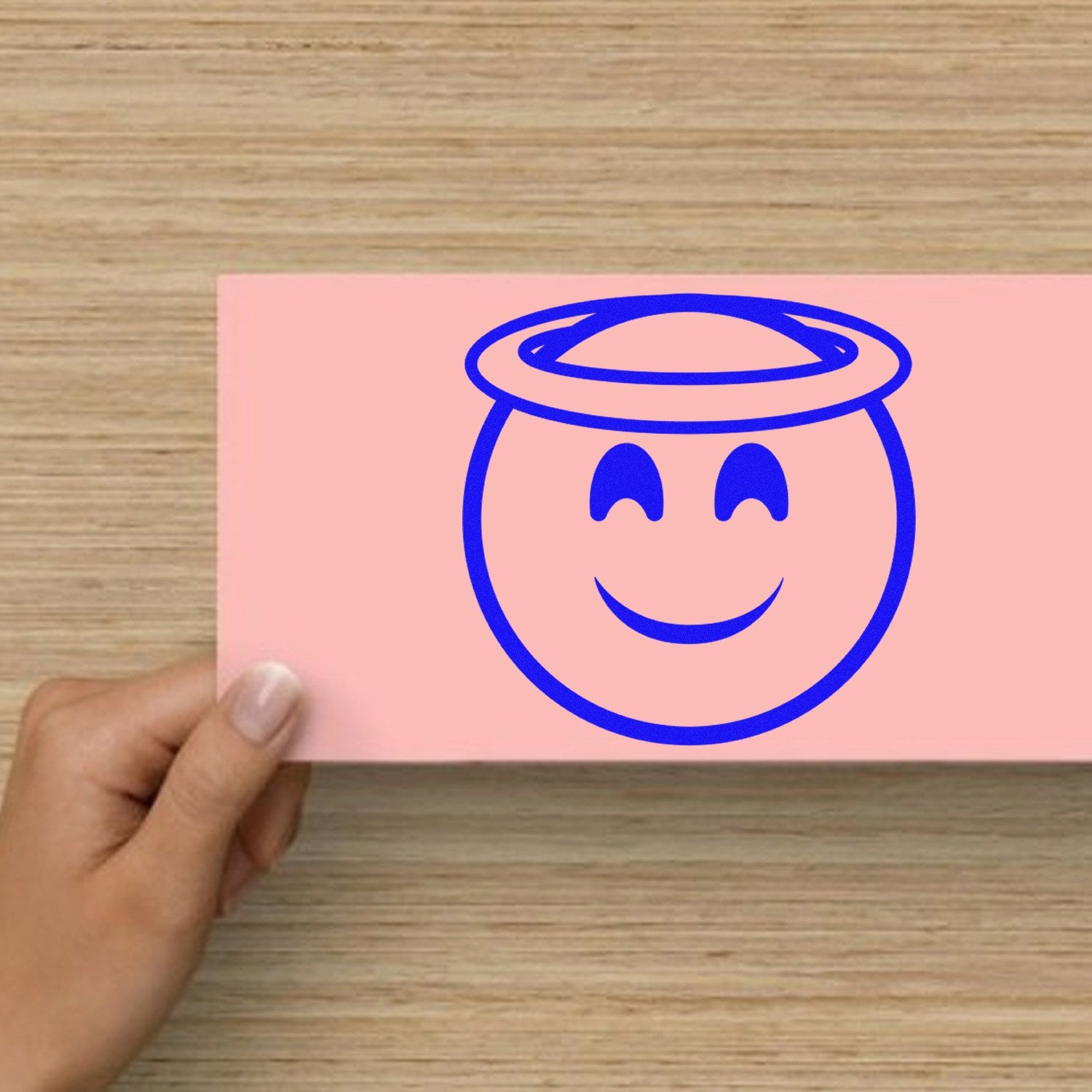 Wood Handle Halo Happiness Emoji Rubber Stamp on a wooden surface, featuring a smiling face with a halo in blue ink. Perfect for adding cheerful touches to crafts and stationery.