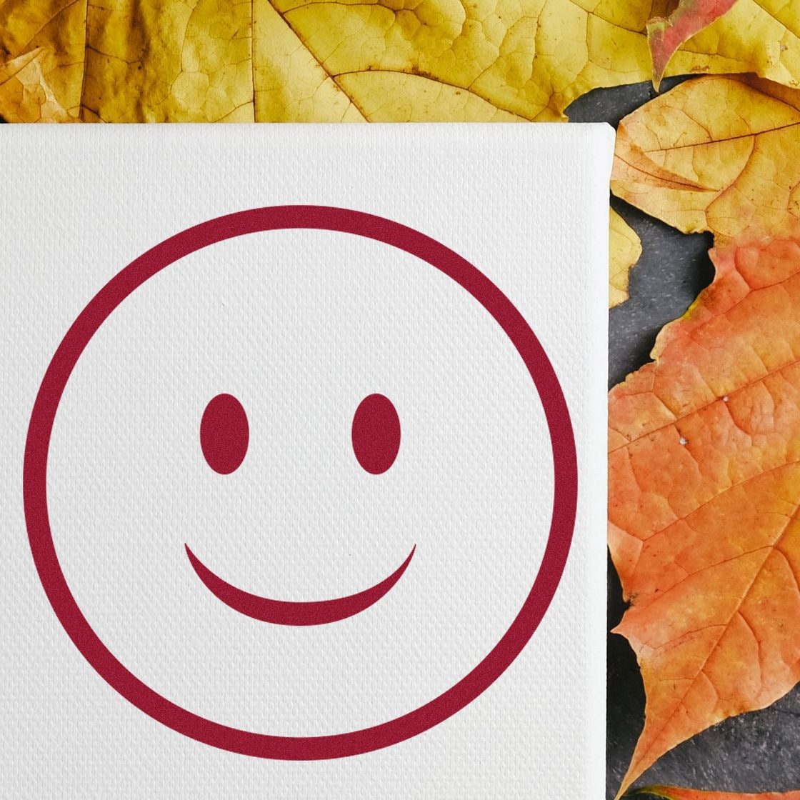 Self-Inking Simple Smiley Emoji Stamp on white canvas, surrounded by autumn leaves. Perfect for adding cheerful touches to crafts and stationery.